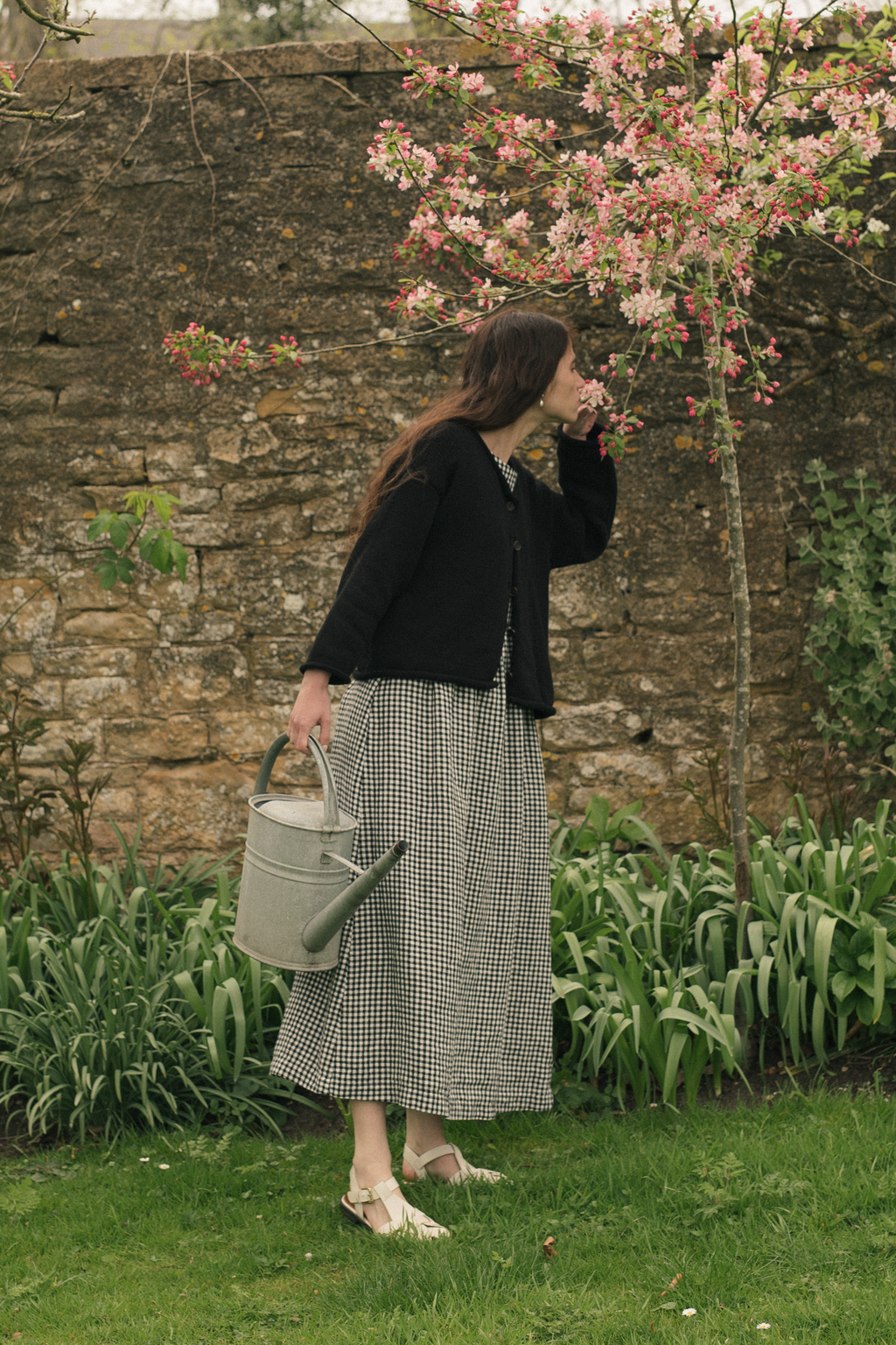Model wearing the Lennon Cardigan in Noir by Gillian Stevens, side view in a garden setting
