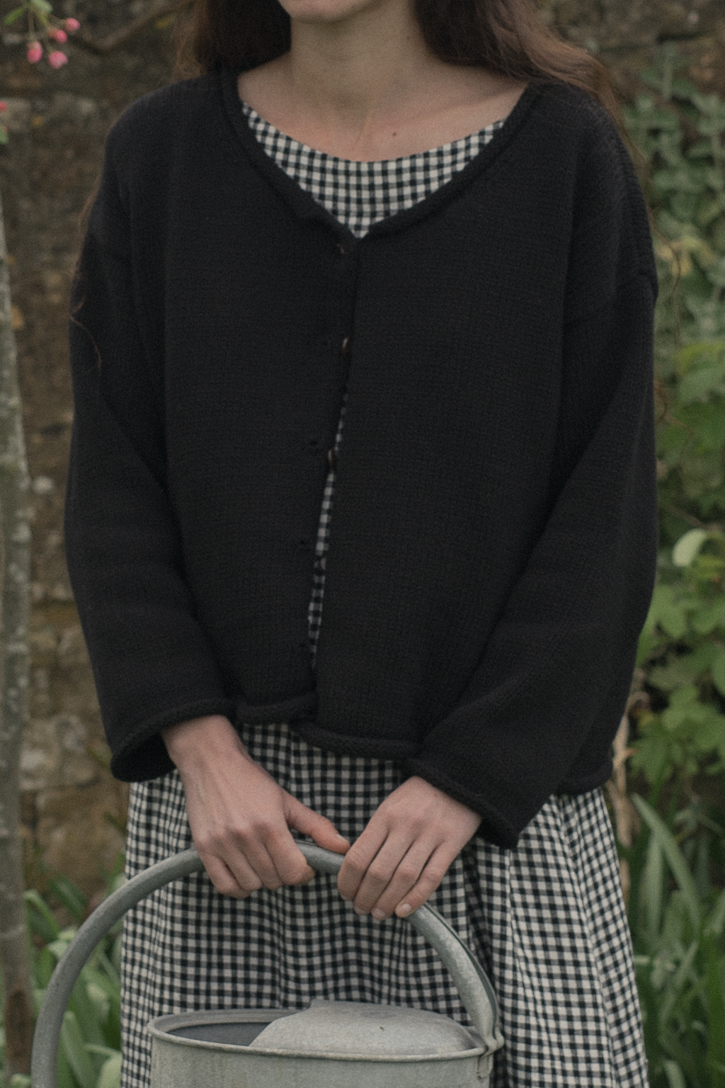 Model wearing the Lennon Cardigan in Noir by Gillian Stevens, front view in a garden setting