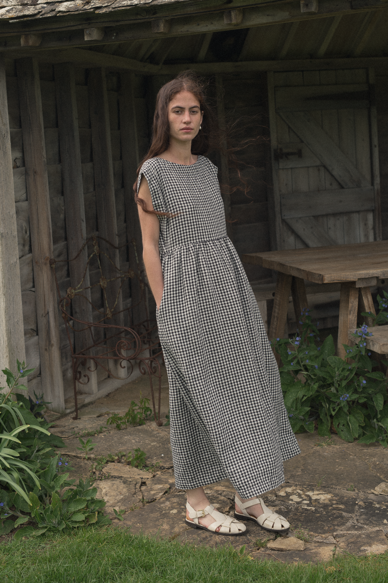 Woman in a checkered dress, the valley dress in gingham noir by Gillian Stevens, standing in front of a shed.
