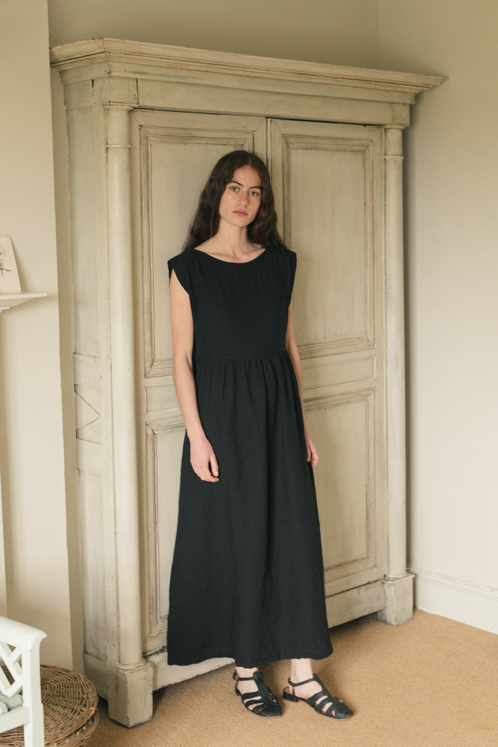 Model wearing the Valley Dress in Noir by Gillian Stevens, front view beside an antique armoire