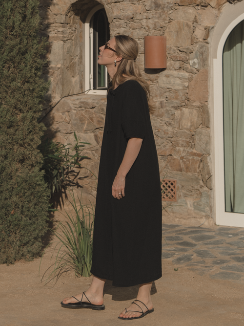 Model wearing the Blair Dress in Noir by Gillian Stevens, side view against stone building