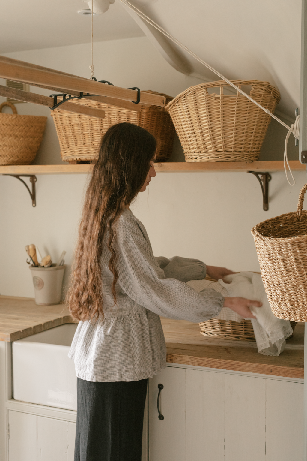 Model wearing the Darla Blouse in Dove Check by Gillian Stevens, side view in a rustic laundry room