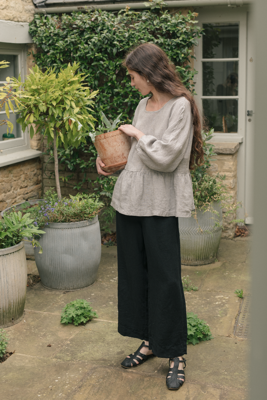 Model wearing the Darla Blouse in Dove Check by Gillian Stevens, three-quarter view in a garden courtyard