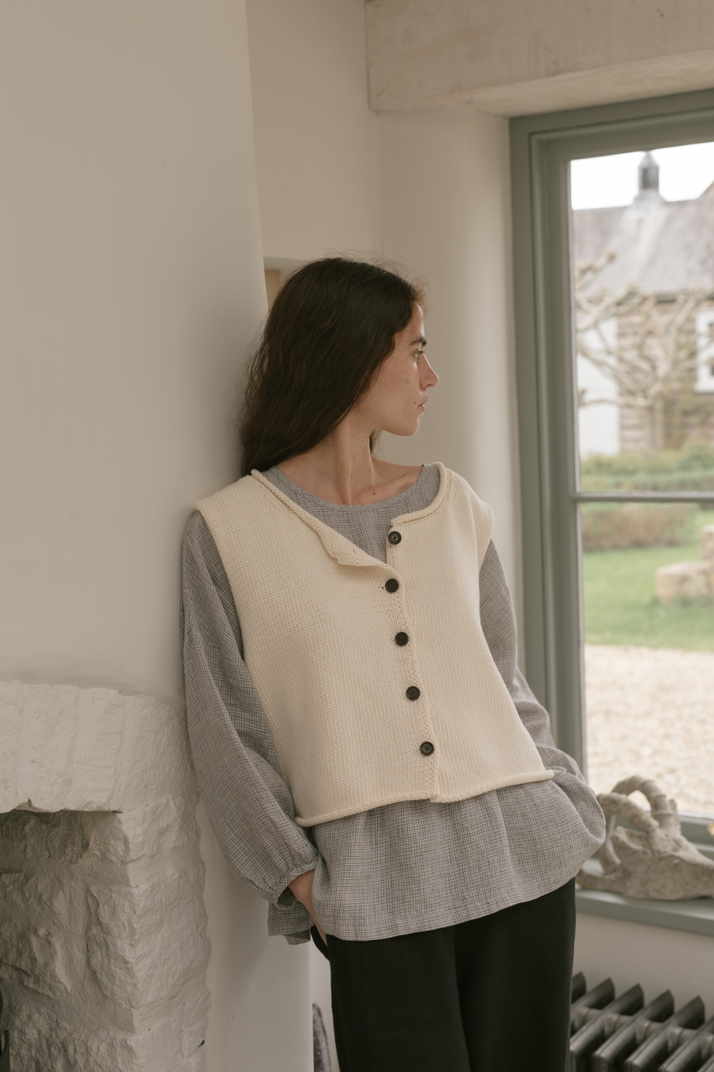 Model wearing the Lennon Vest in Ivory by Gillian Stevens, side profile view near a window