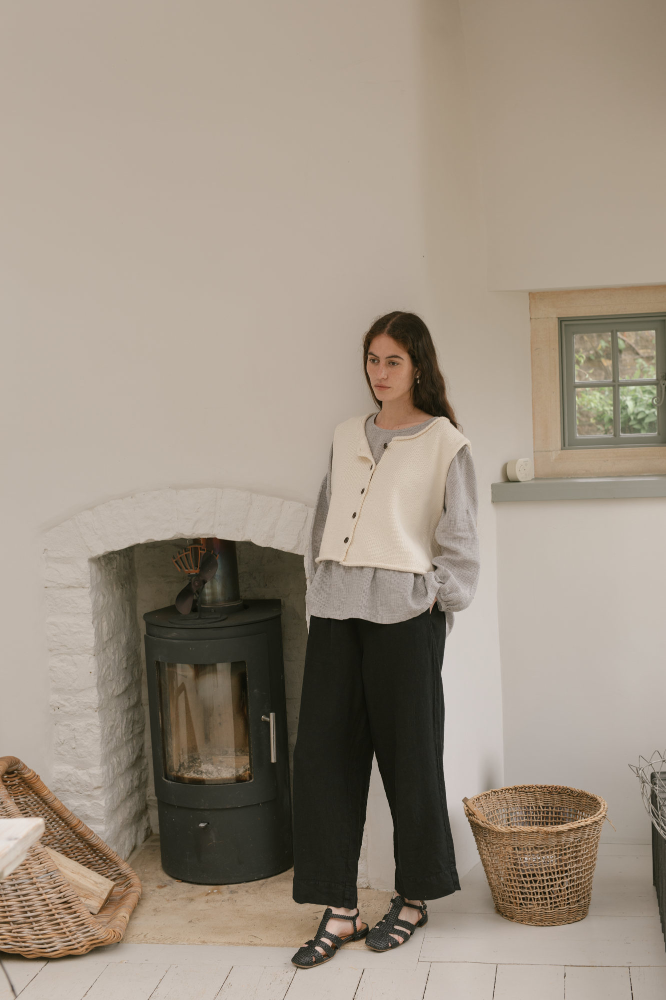 Model wearing the Lennon Vest in Ivory by Gillian Stevens, full-length front view beside a wood burner