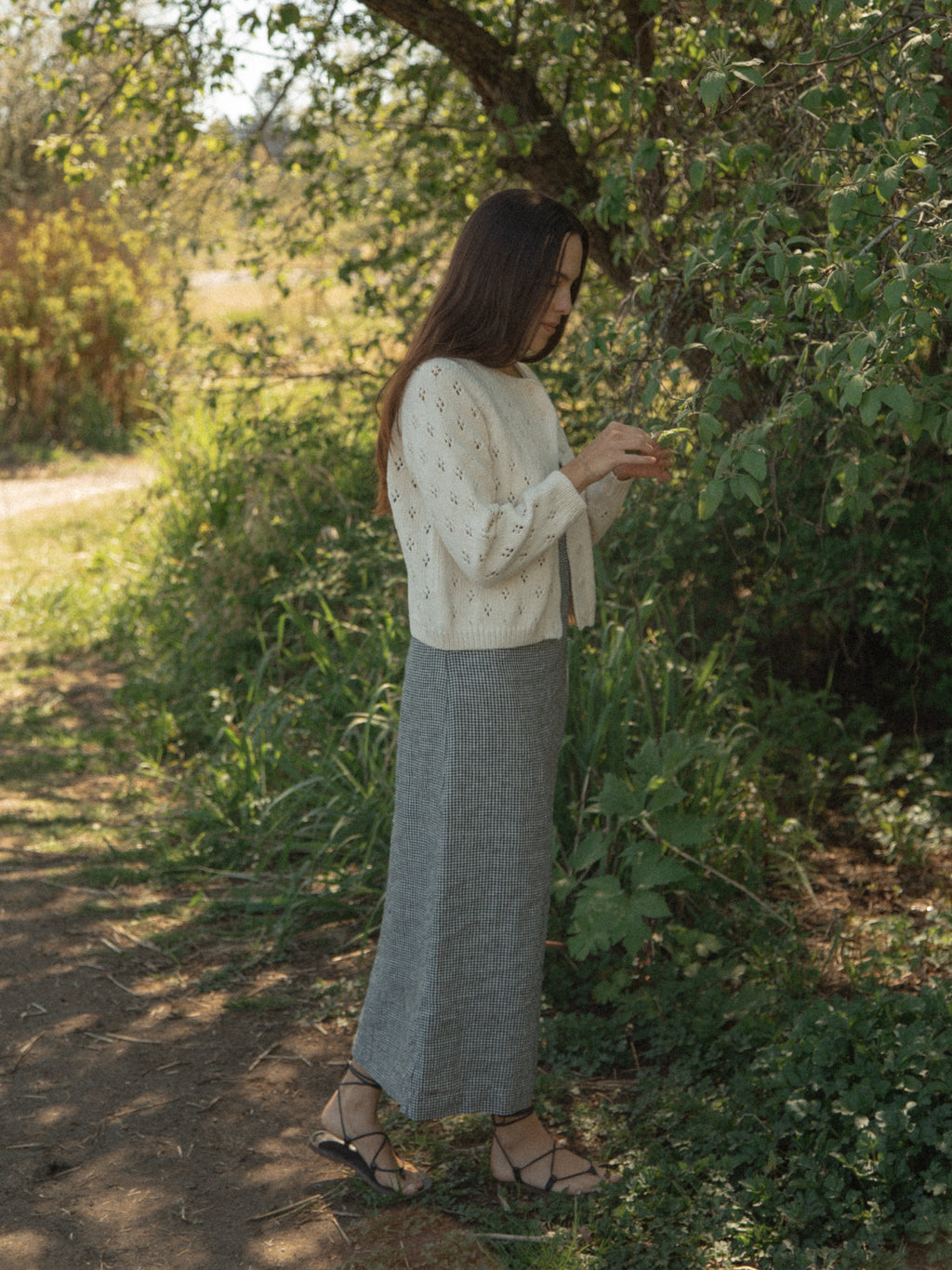Model wearing the Mabel Cardigan in Ivory by Gillian Stevens, side view on a sunlit nature path