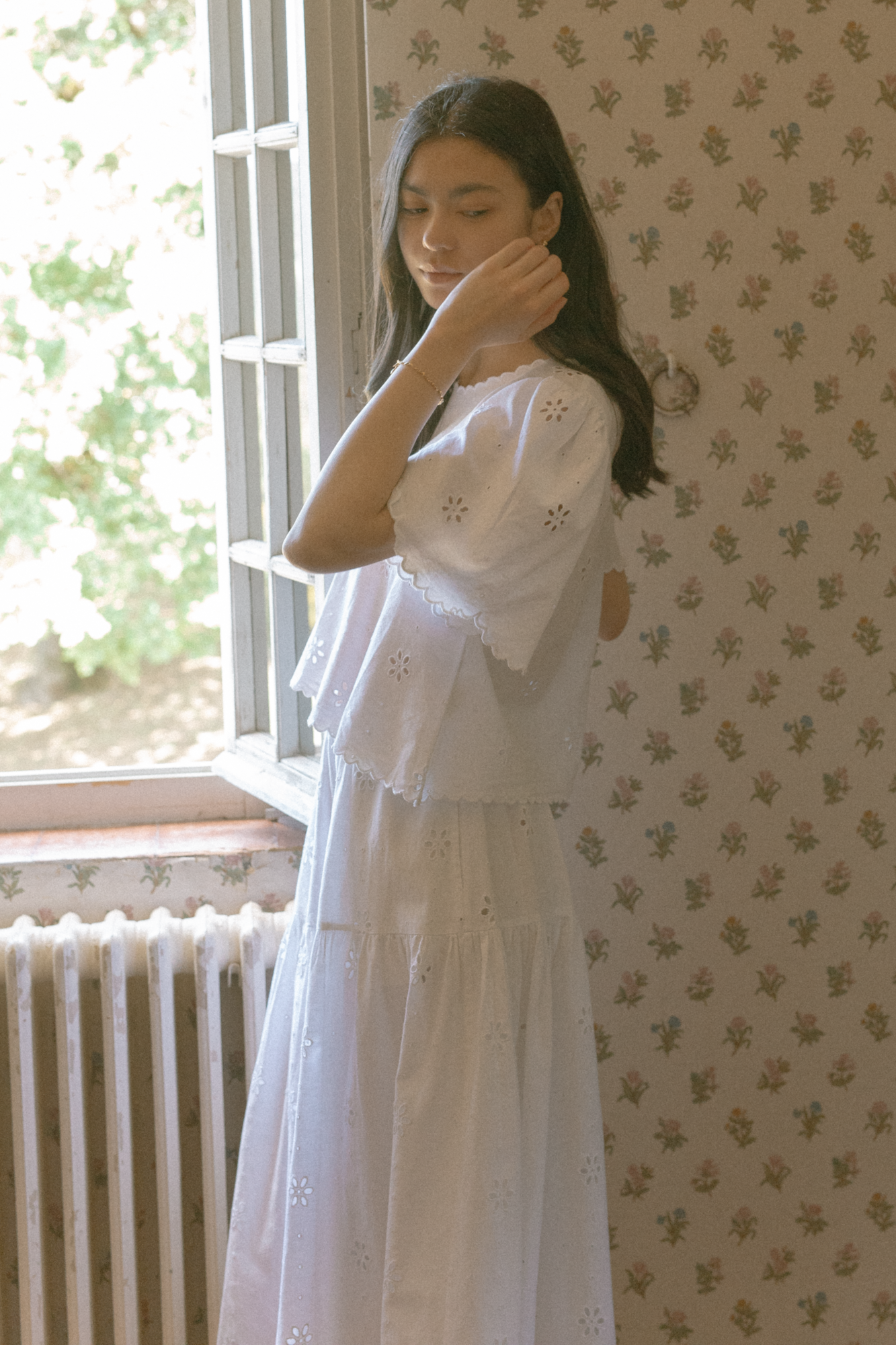 Model wearing the Stella Top in Salt by Gillian Stevens, side view beside a sunlit window with floral wallpaper
