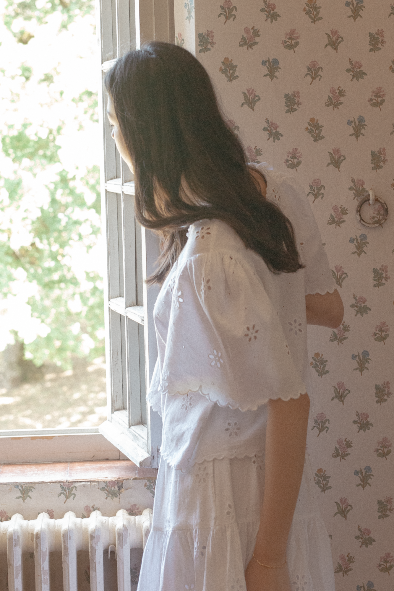 Model in the Stella Top in Salt by Gillian Stevens, side view showing eyelet detail by a window