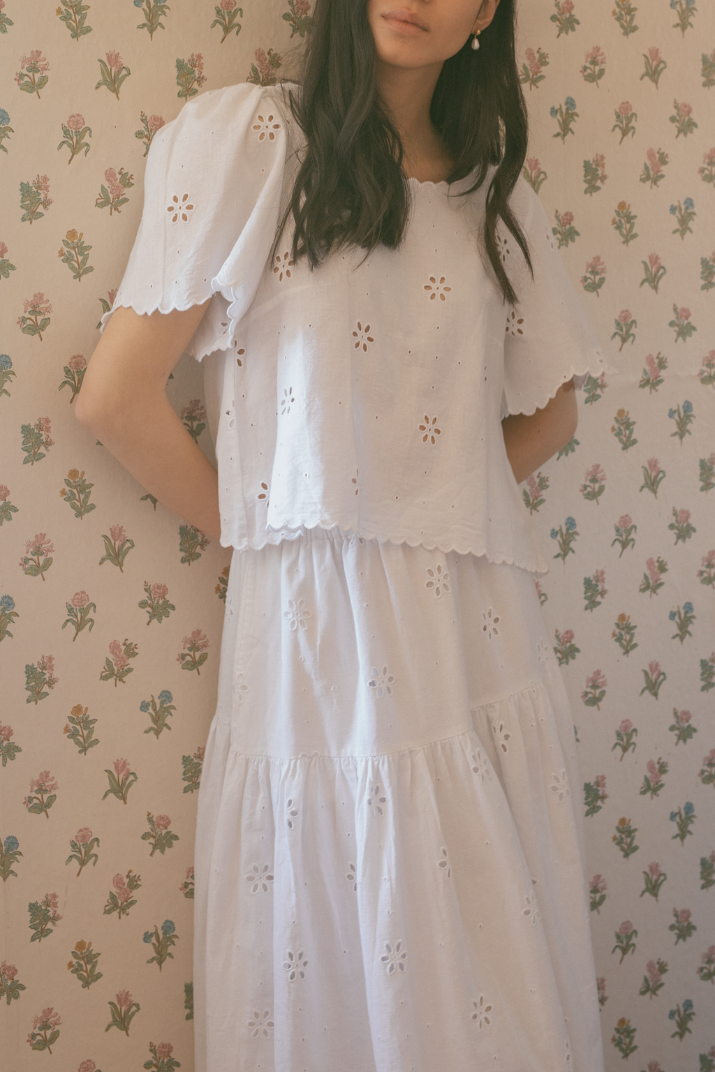Model wearing the Stella Top in Salt by Gillian Stevens, front view showing eyelet detail and scallop hem against floral