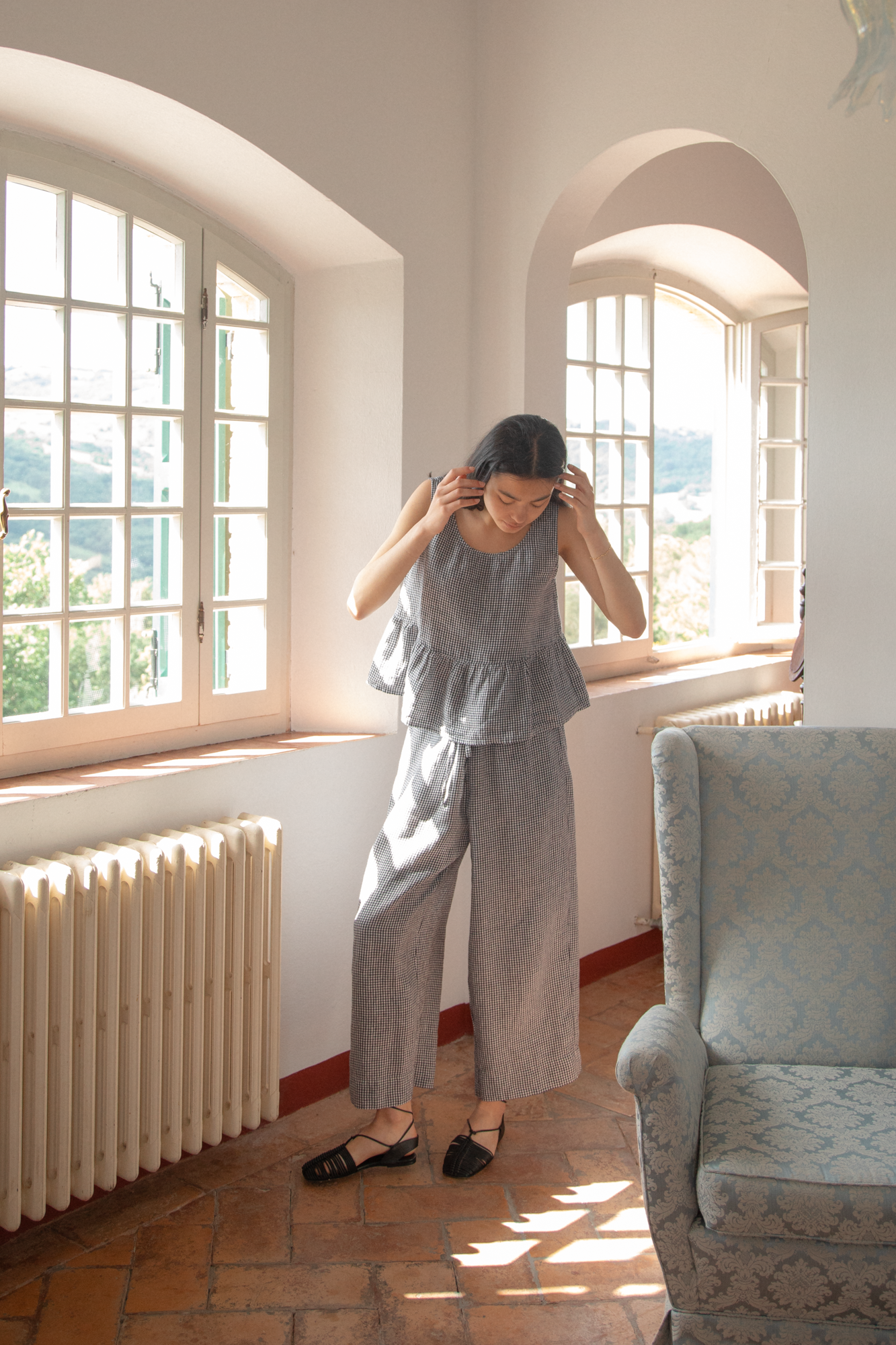 Model wearing the Olive Pant in Marine Gingham by Gillian Stevens, front view in a sunlit European interior