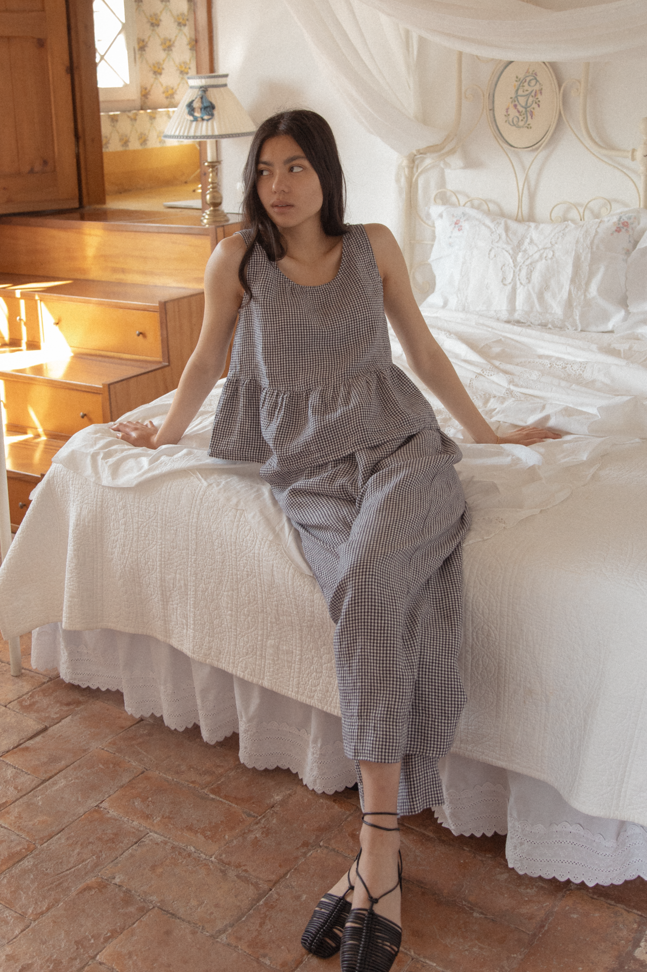 Model wearing the Marlowe Top in Marine Gingham by Gillian Stevens, seated front view in a warmly lit bedroom setting