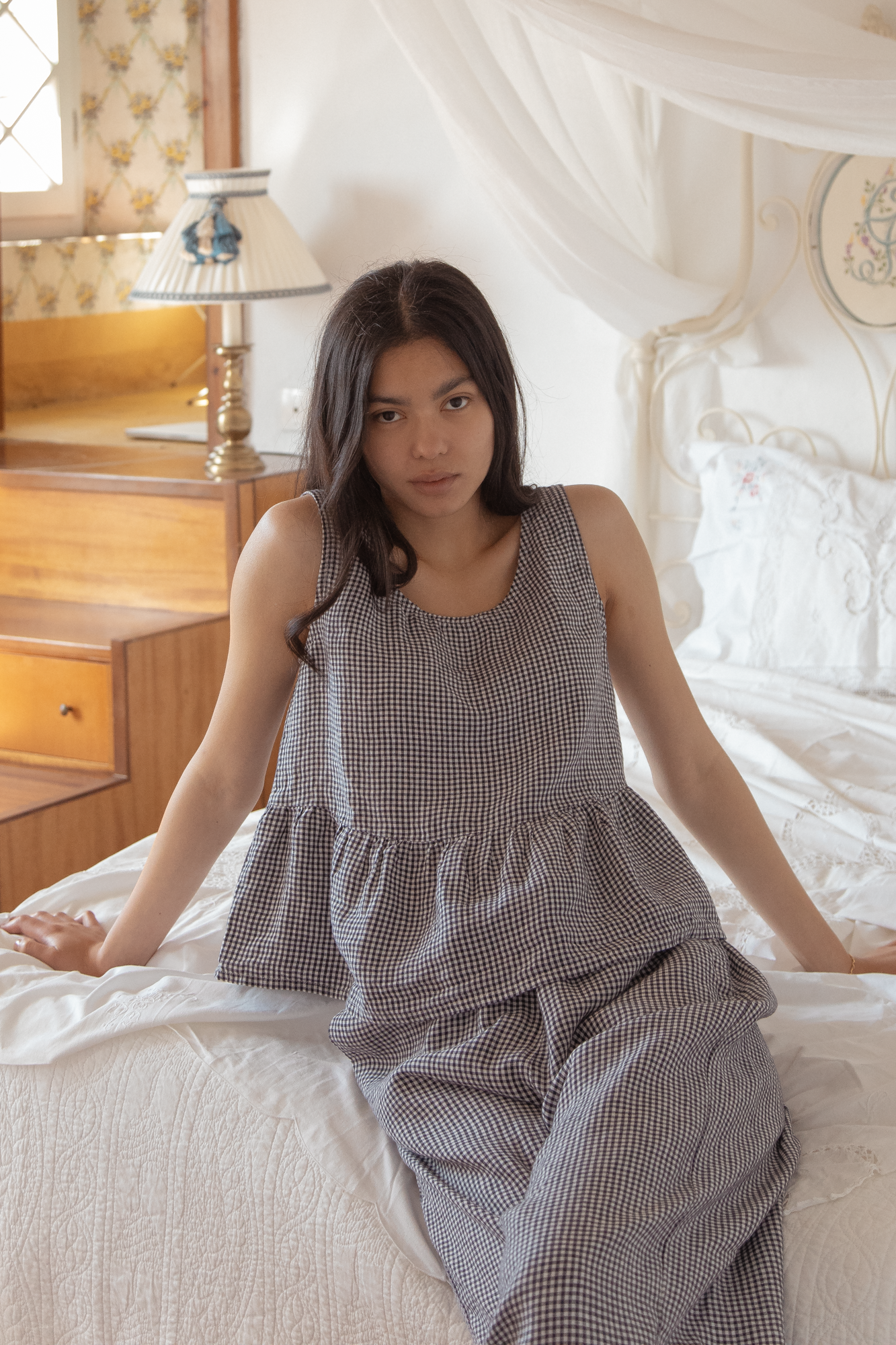 Model seated on a bed wearing the Marlowe Top in Marine Gingham by Gillian Stevens, front view