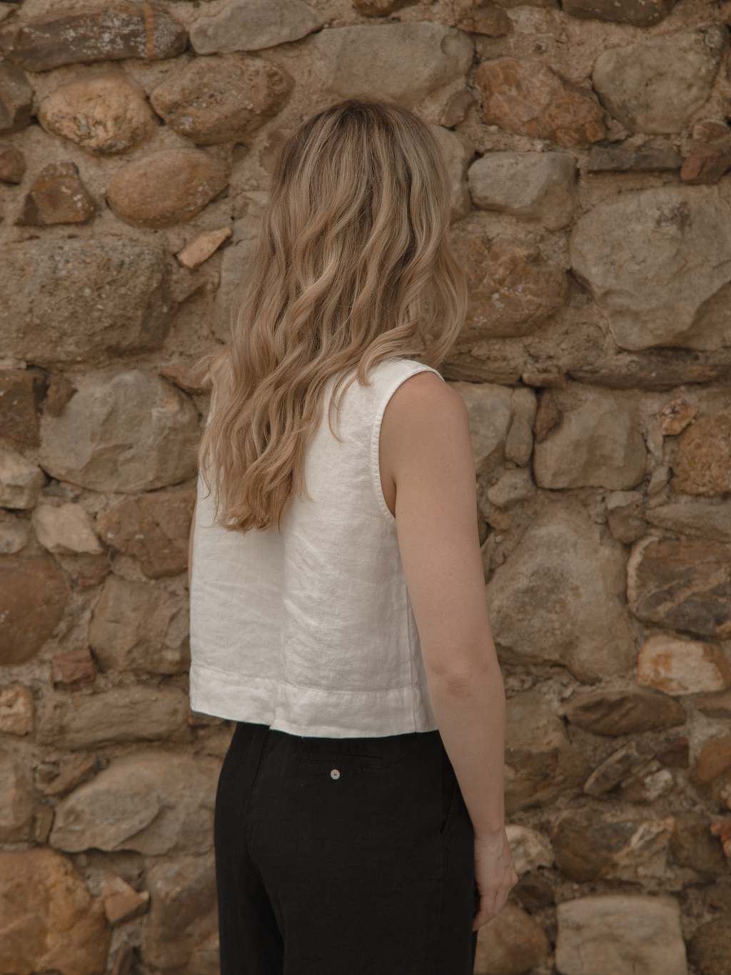 Model wearing the Finley Top in Salt by Gillian Stevens, back view against a stone wall