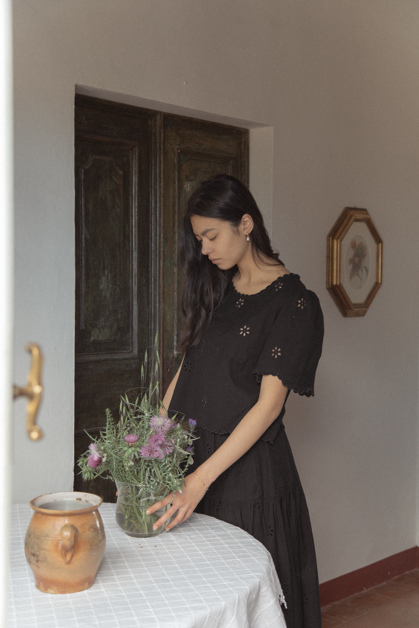 Model wearing the Stella Top in Noir by Gillian Stevens, front view styled with a black skirt in a rustic interior