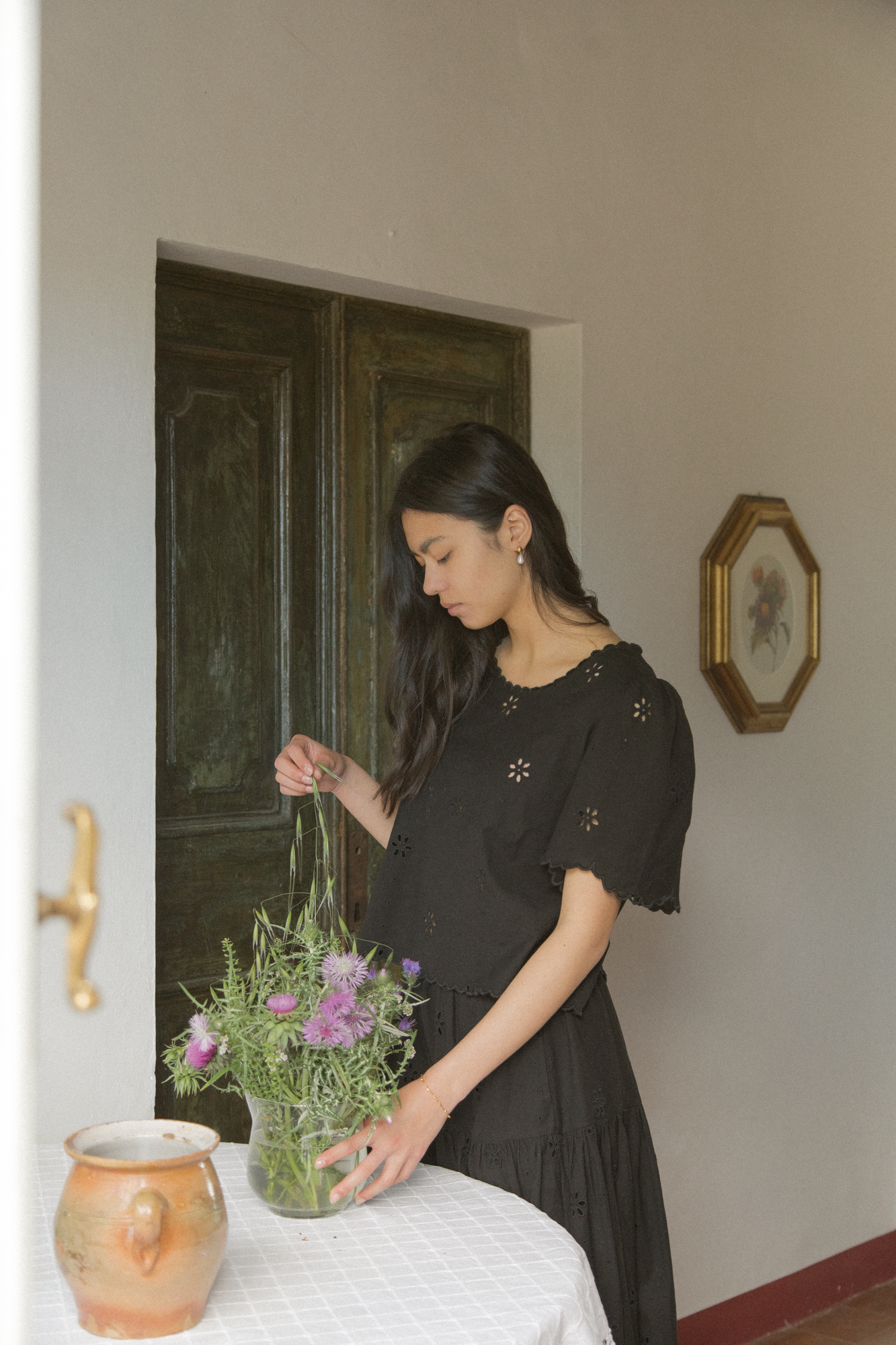 Model wearing the Stella Top in Noir by Gillian Stevens, arranging wildflowers in a rustic interior setting