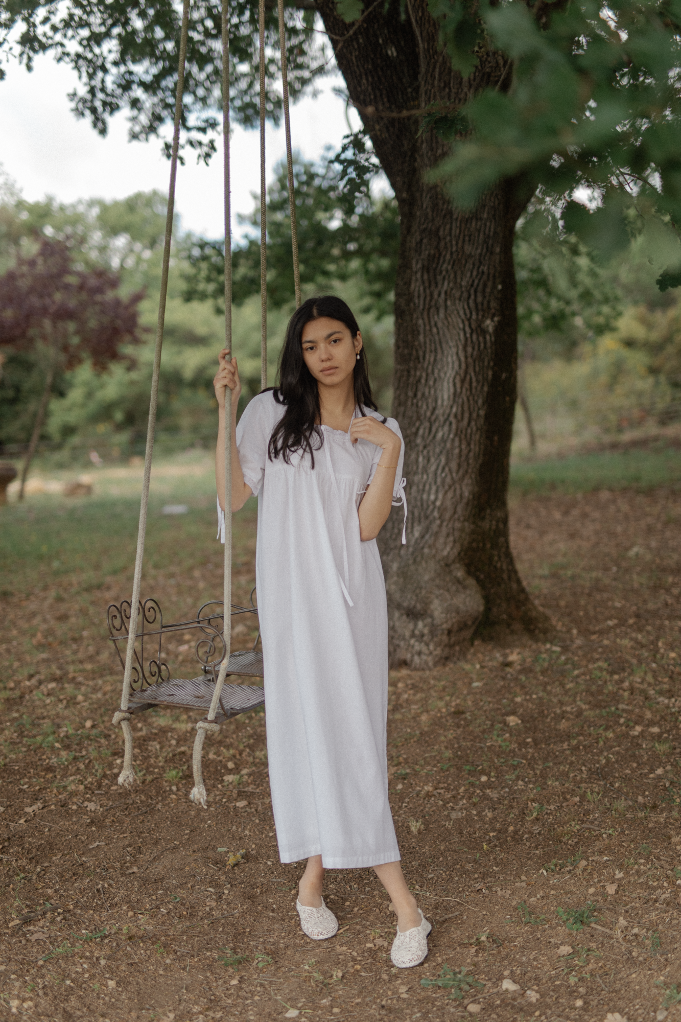 Model wearing the Dace Dress in Salt by Gillian Stevens, standing beside a tree swing outdoors