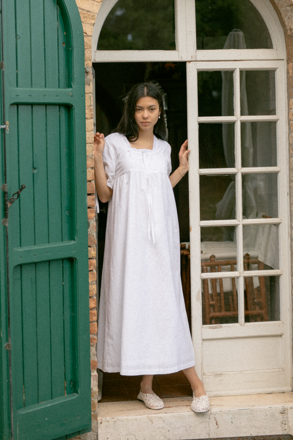 Model wearing the Dace Dress in Salt by Gillian Stevens, front view framed by a rustic arched doorway