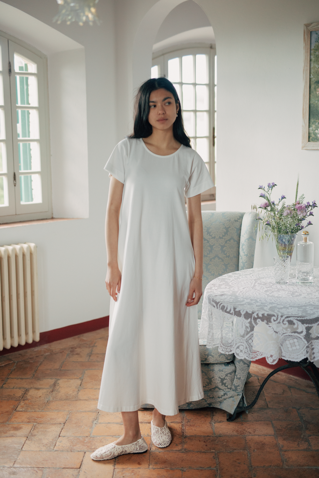 Model wearing the Palmer Dress in Salt by Gillian Stevens, front view in a sunlit European interior