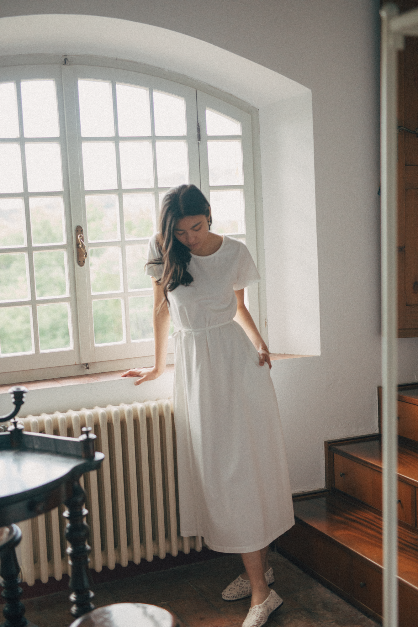 Model wearing the Palmer Dress in Salt by Gillian Stevens, front view in a sunlit room by an arched window