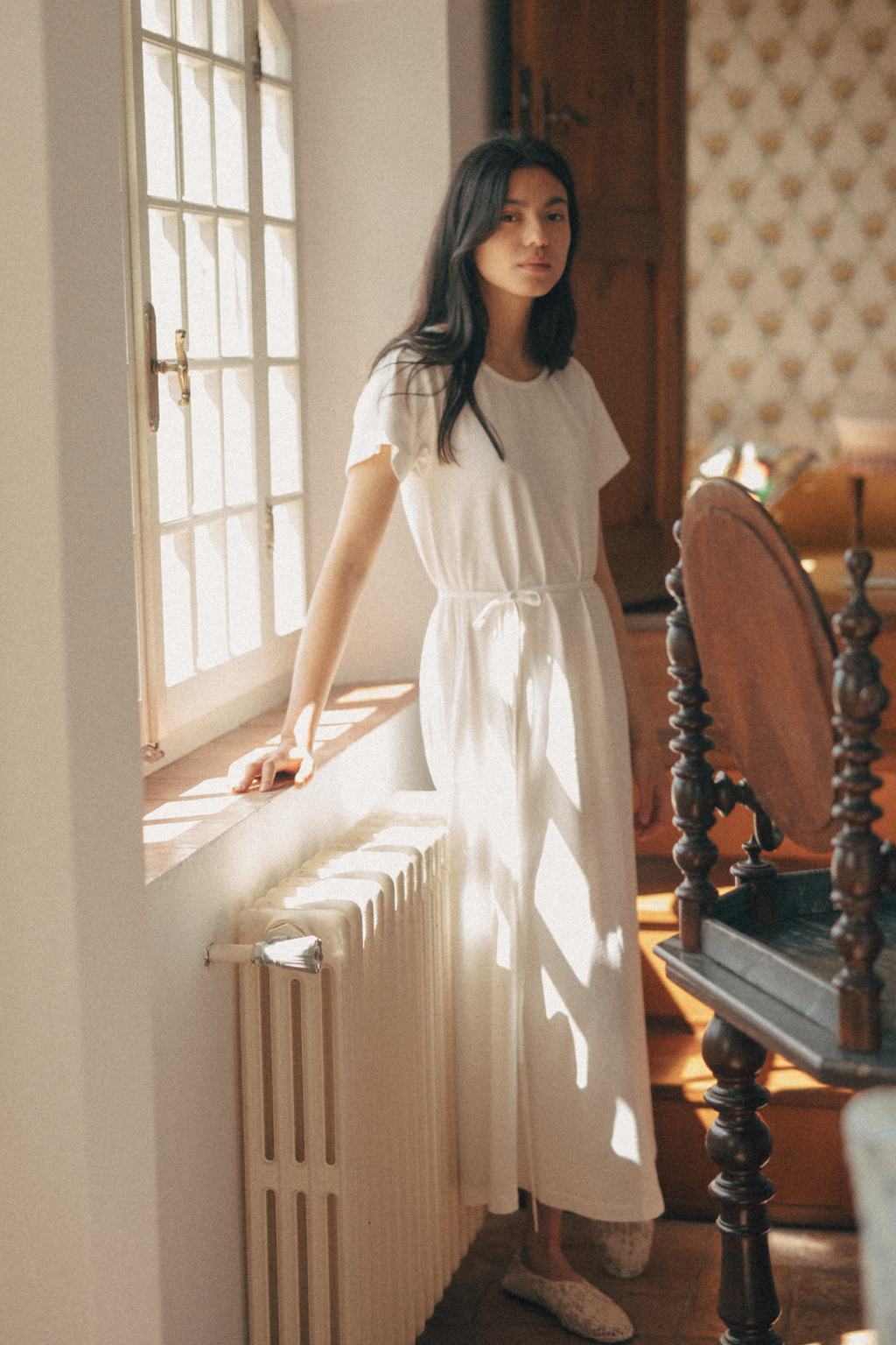 Model wearing the Palmer Dress in Salt by Gillian Stevens, standing by a sunlit window in a vintage interior