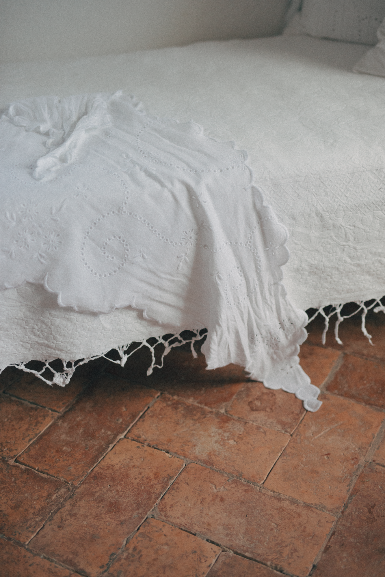 The Matilde Scarf in Salt by Gillian Stevens, draped over a bed showing broderie detail and scalloped edge