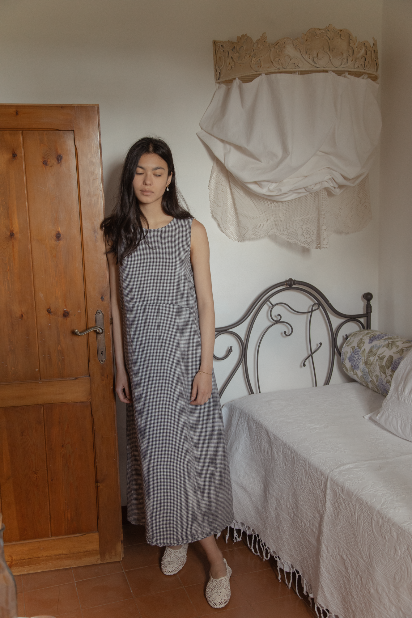 Model wearing the Paige Dress in Marine Gingham by Gillian Stevens, front view in a rustic bedroom setting
