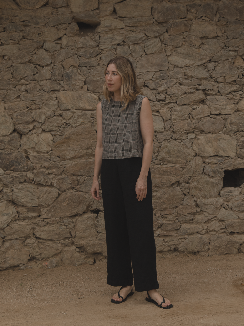 Model wearing the Finley Top in Grey Plaid by Gillian Stevens, front view against stone wall