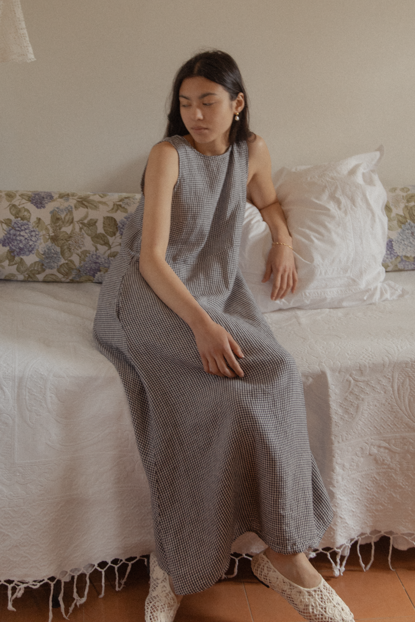 Model seated on a bed wearing the Paige Dress in Marine Gingham by Gillian Stevens, front view