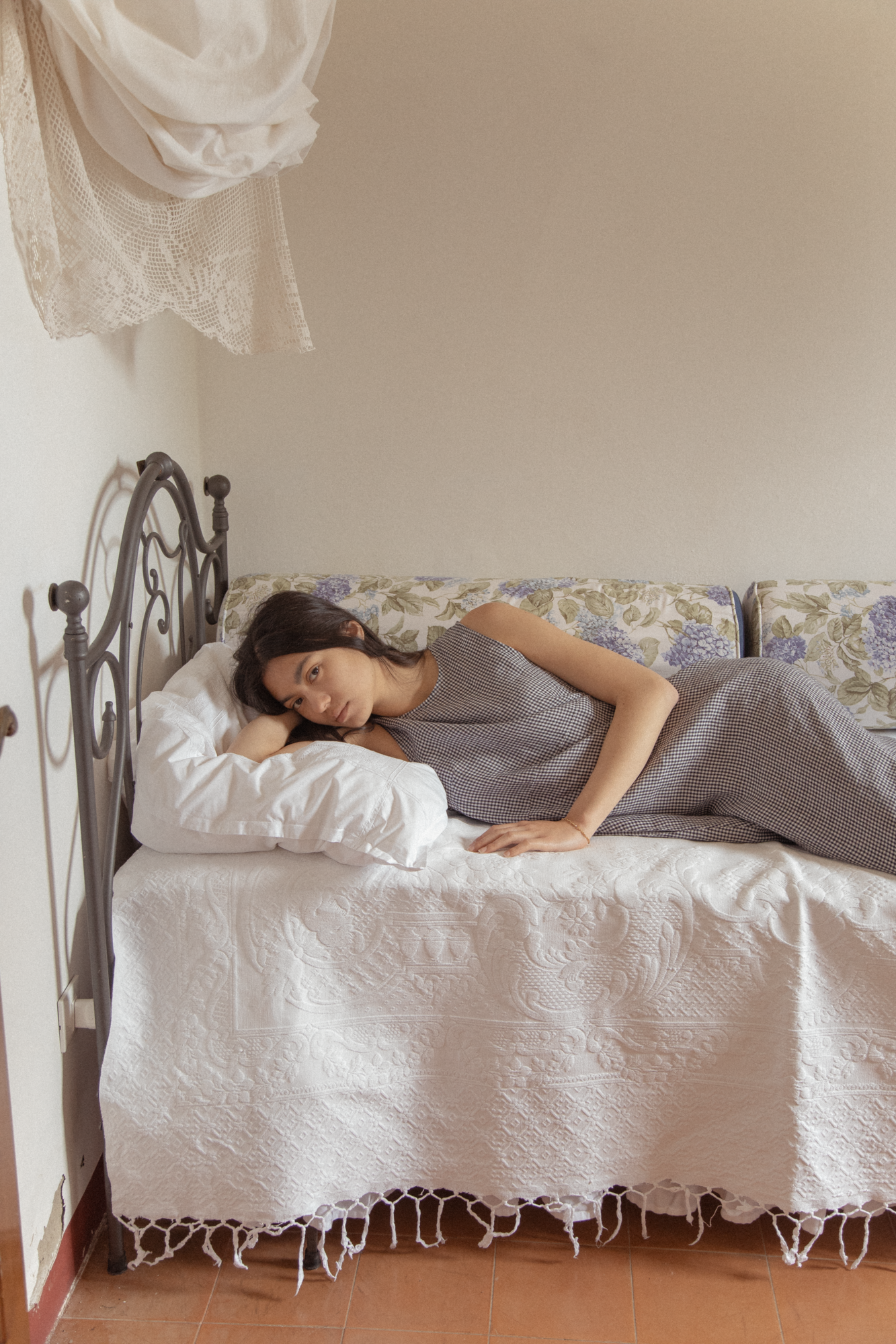 Model wearing the Paige Dress in Marine Gingham by Gillian Stevens, reclining on a vintage daybed
