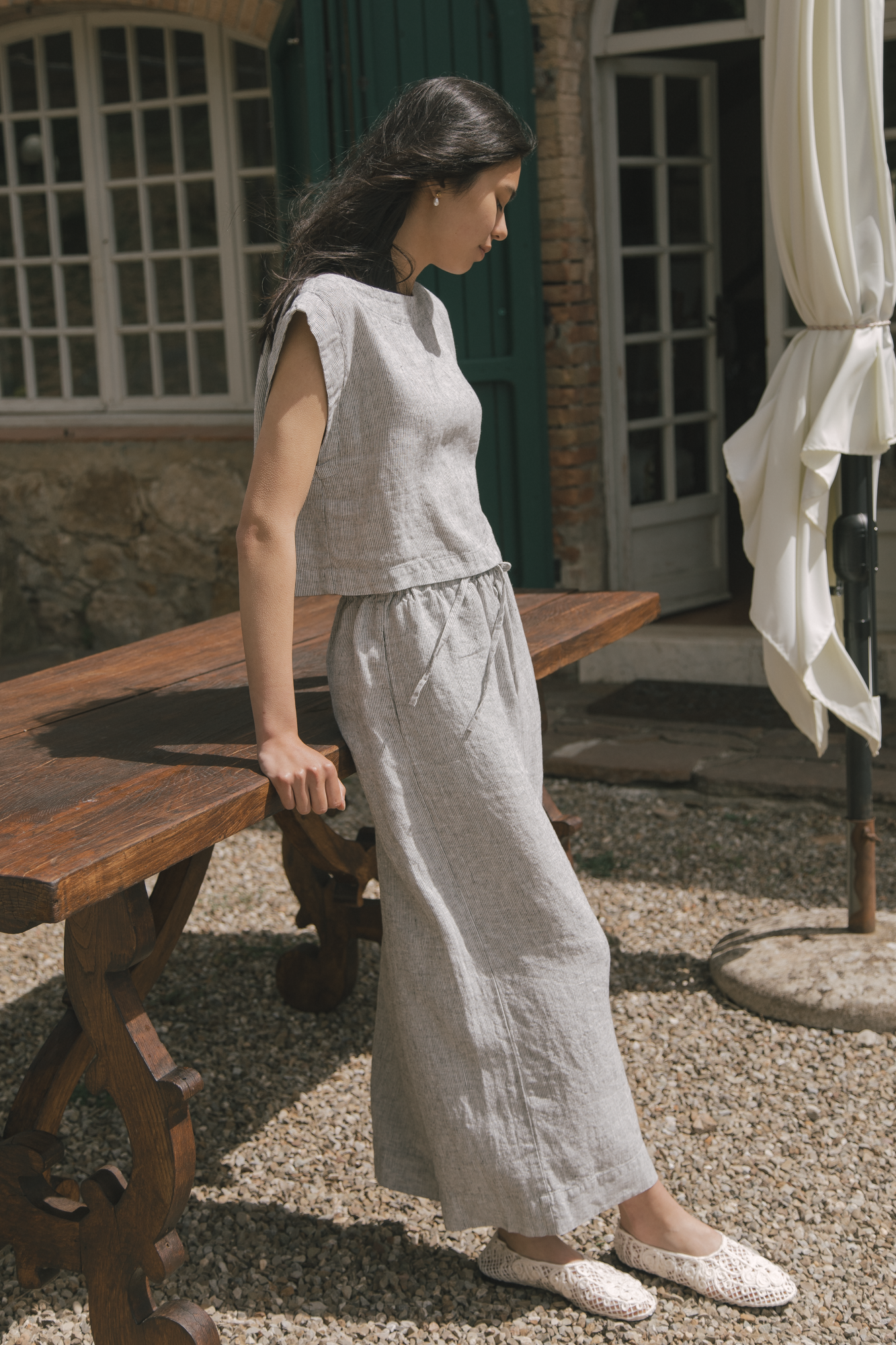 Model wearing the Ines Pant in Charcoal Stripe by Gillian Stevens, side view in a sunlit courtyard