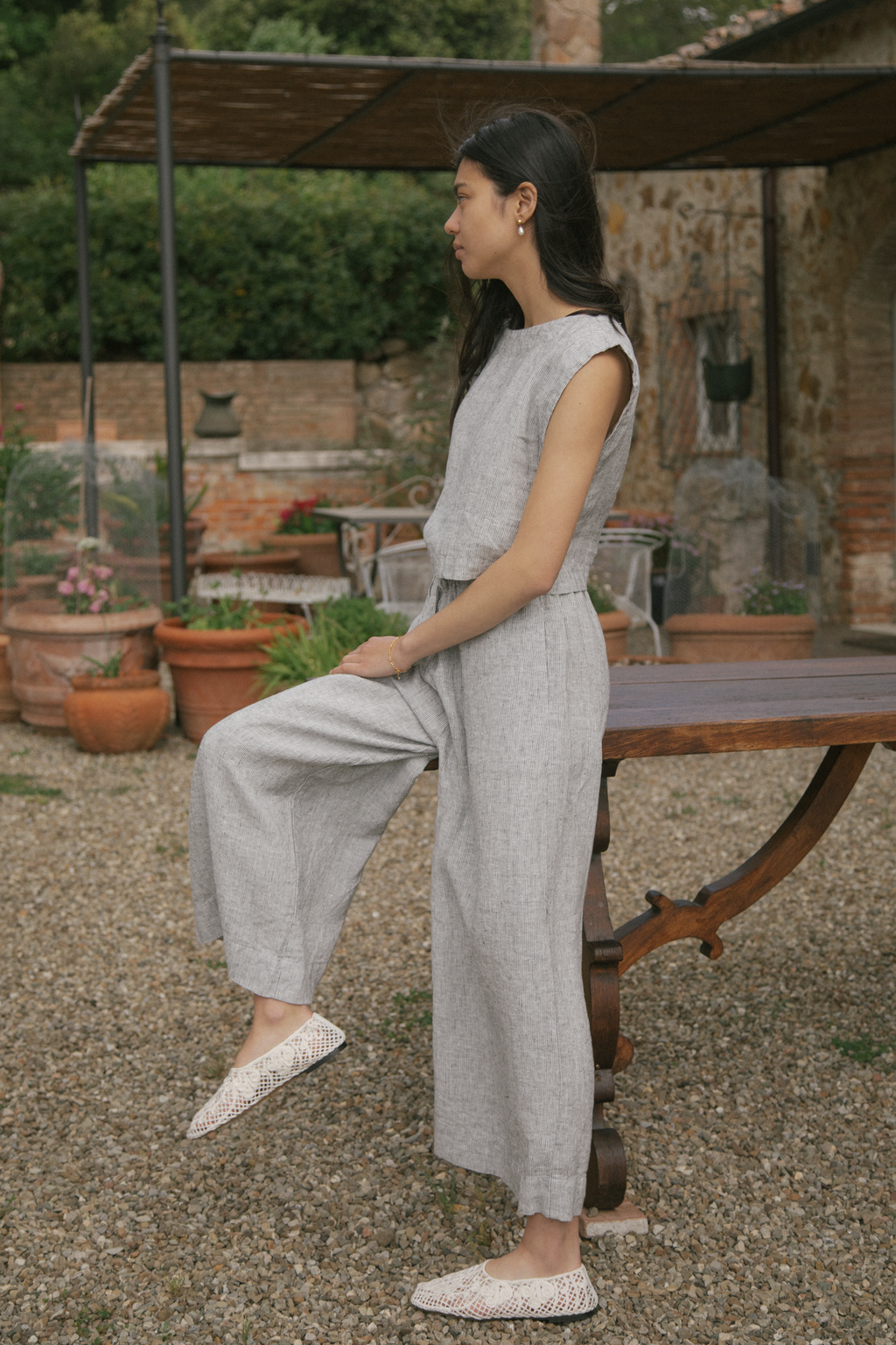 Model in the Ines Pant in Charcoal Stripe by Gillian Stevens, side view seated outdoors on a rustic table