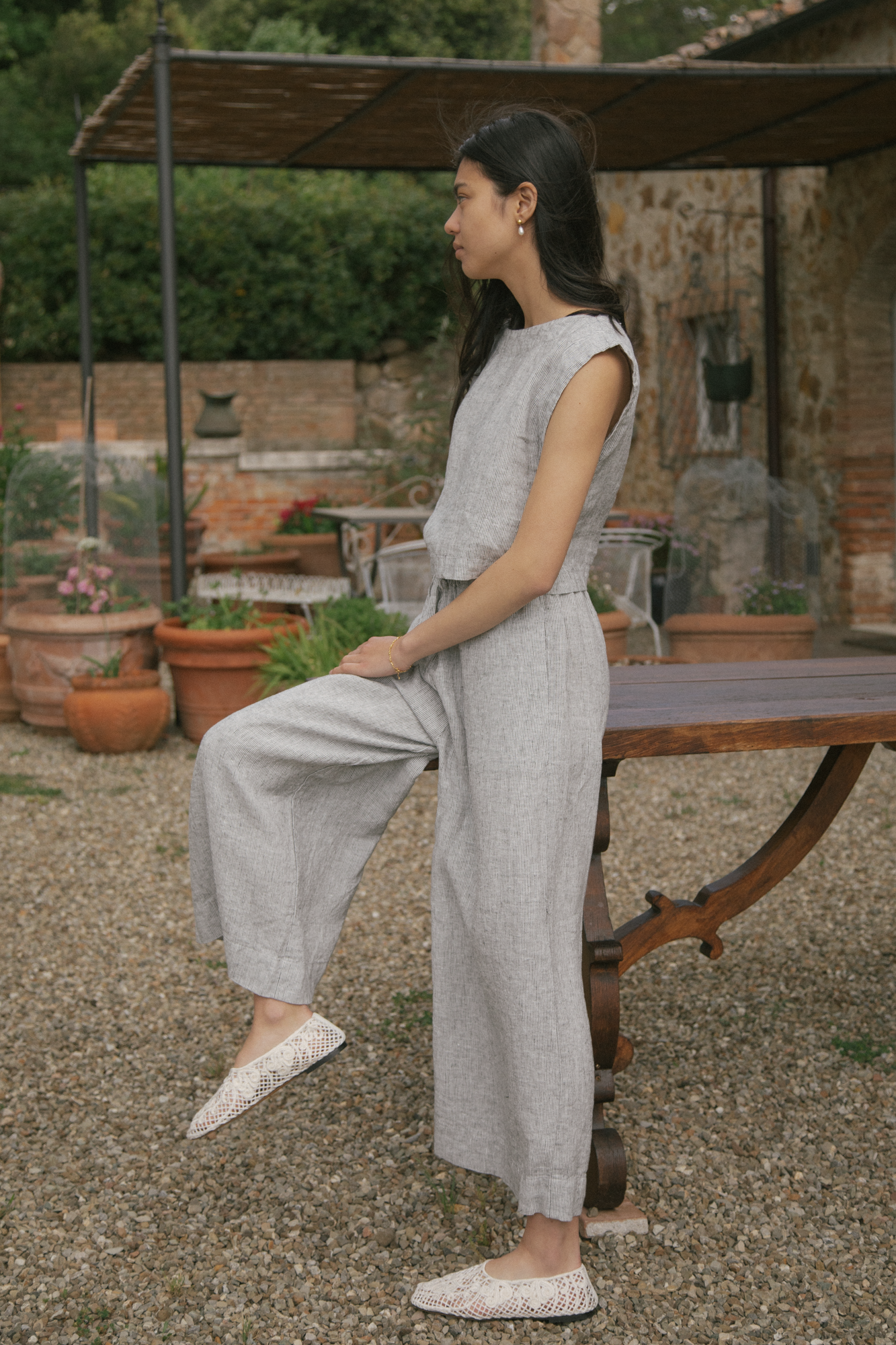 Model in the Ines Pant in Charcoal Stripe by Gillian Stevens, side view seated outdoors on a rustic table
