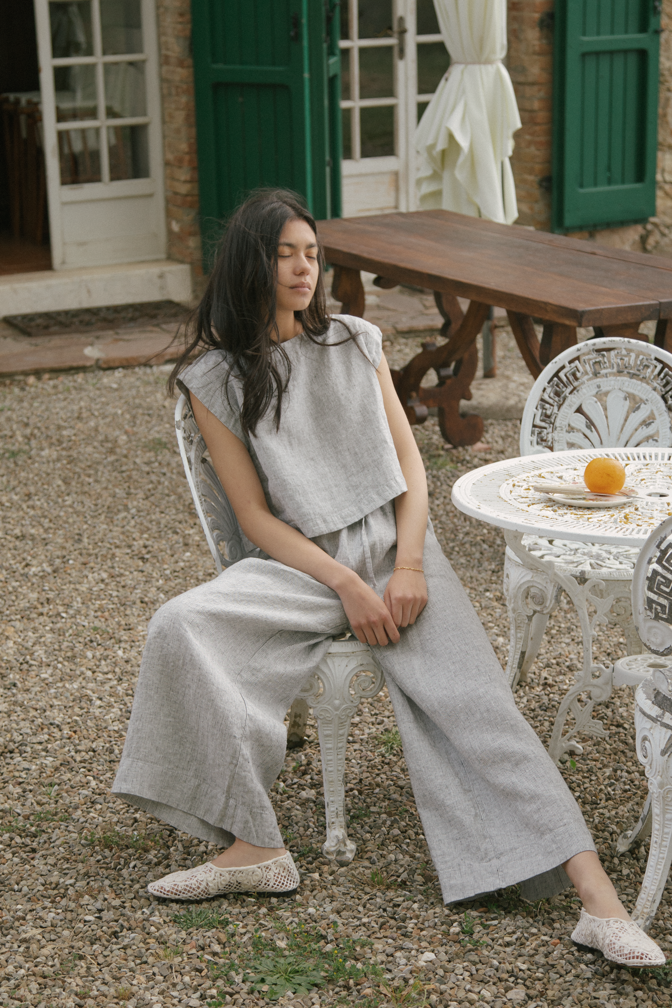 Model seated outdoors in the Ines Pant Charcoal Stripe by Gillian Stevens, showing wide leg and linen texture