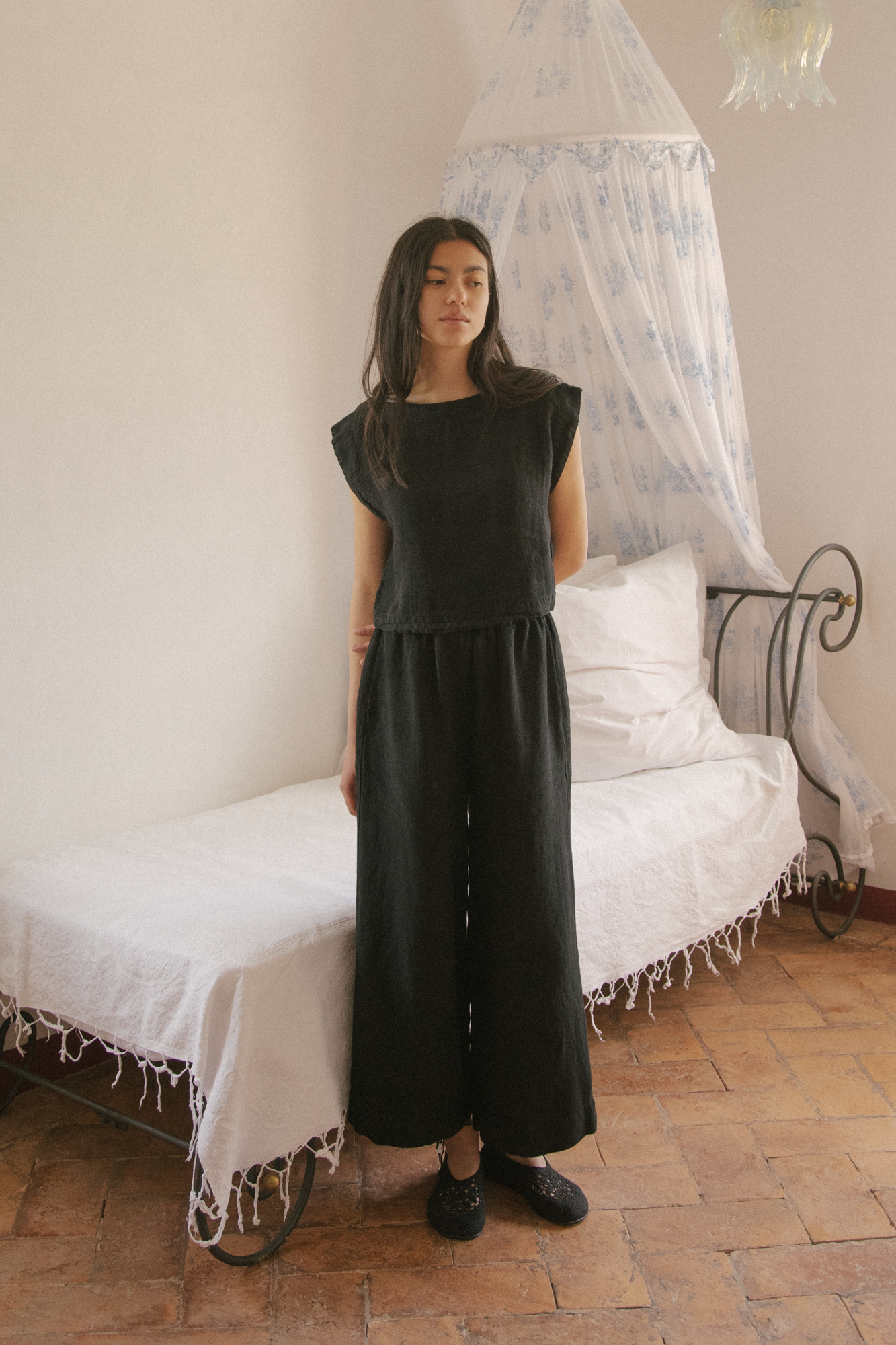 Model wearing the Valley Top in Noir by Gillian Stevens, front view styled with wide-leg pants in a bedroom setting