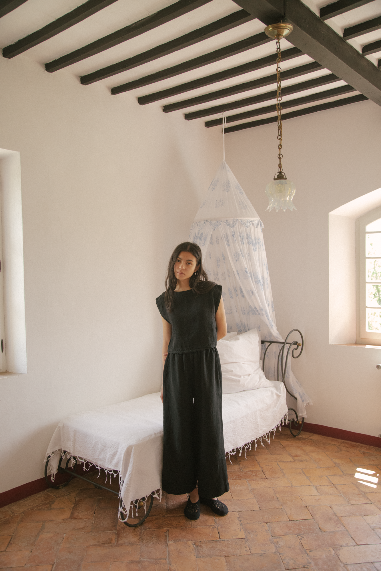 Model wearing the Ines Pant in Noir by Gillian Stevens, full-length front view in a rustic beamed room