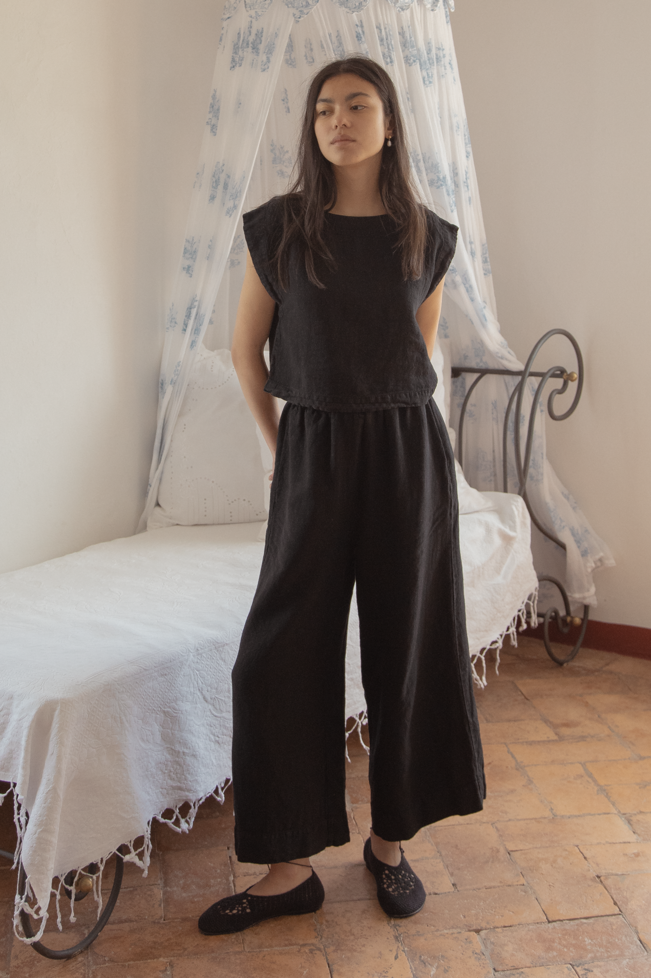 Model wearing the Valley Top in Noir by Gillian Stevens, styled with wide-leg black pants, front view in a bedroom setting