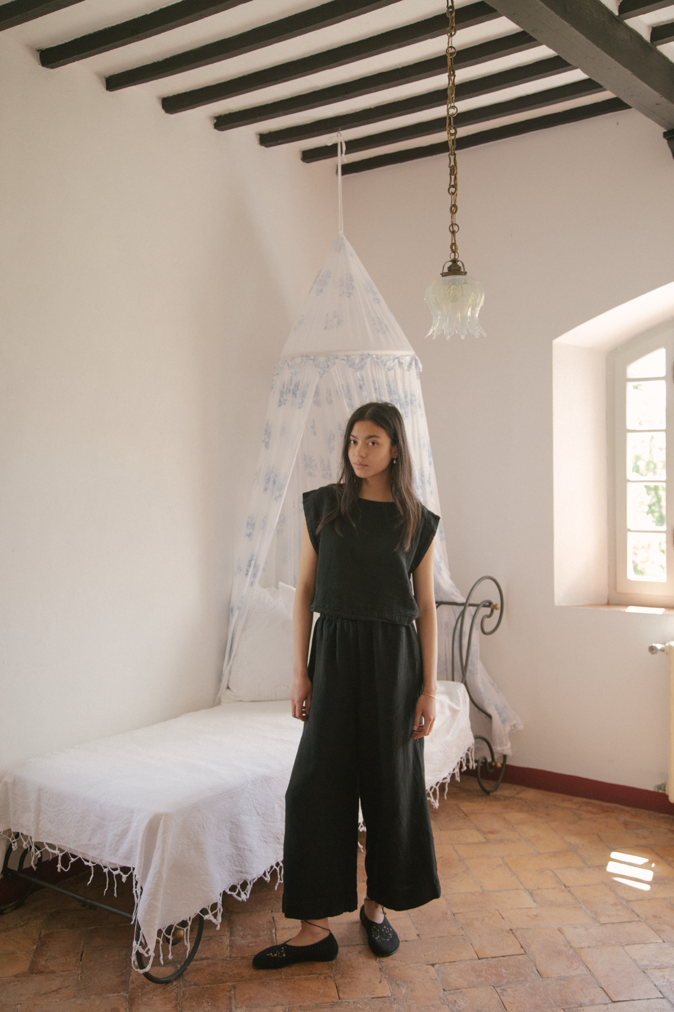Model wearing the Ines Pant in Noir by Gillian Stevens, full-length front view in a rustic room