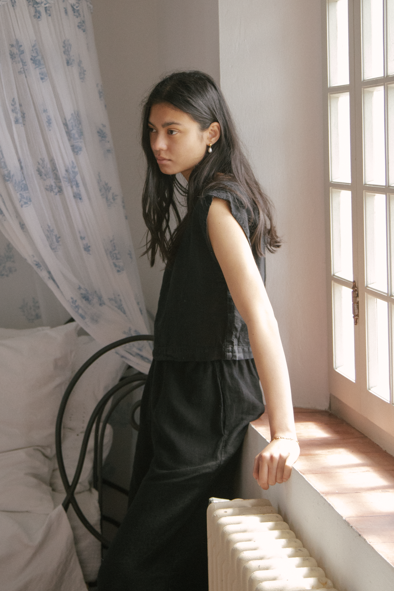 Model wearing the Valley Top in Noir by Gillian Stevens, side view beside a sunlit window