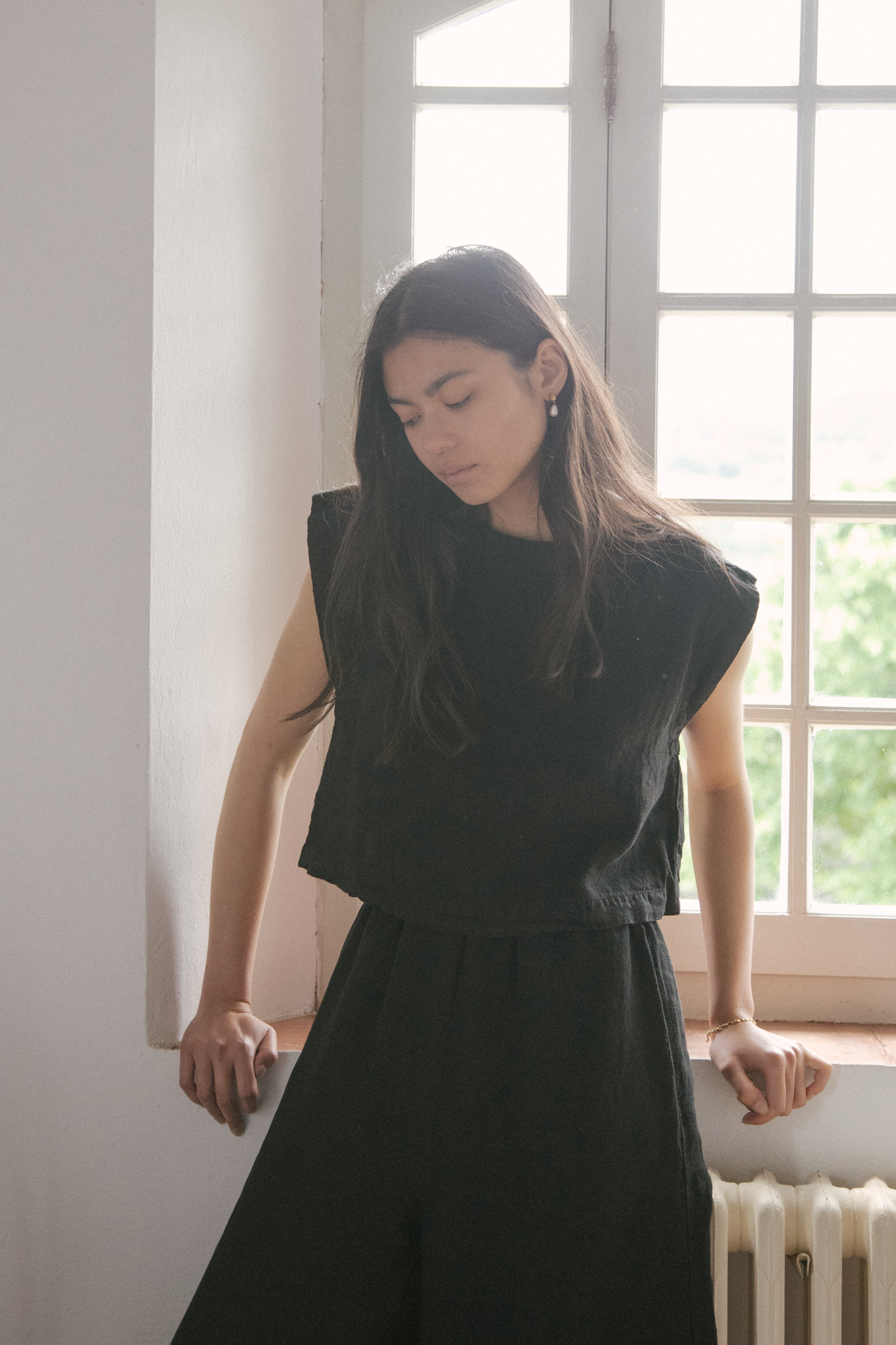 Model wearing the Valley Top in Noir by Gillian Stevens, front view beside a sunlit window