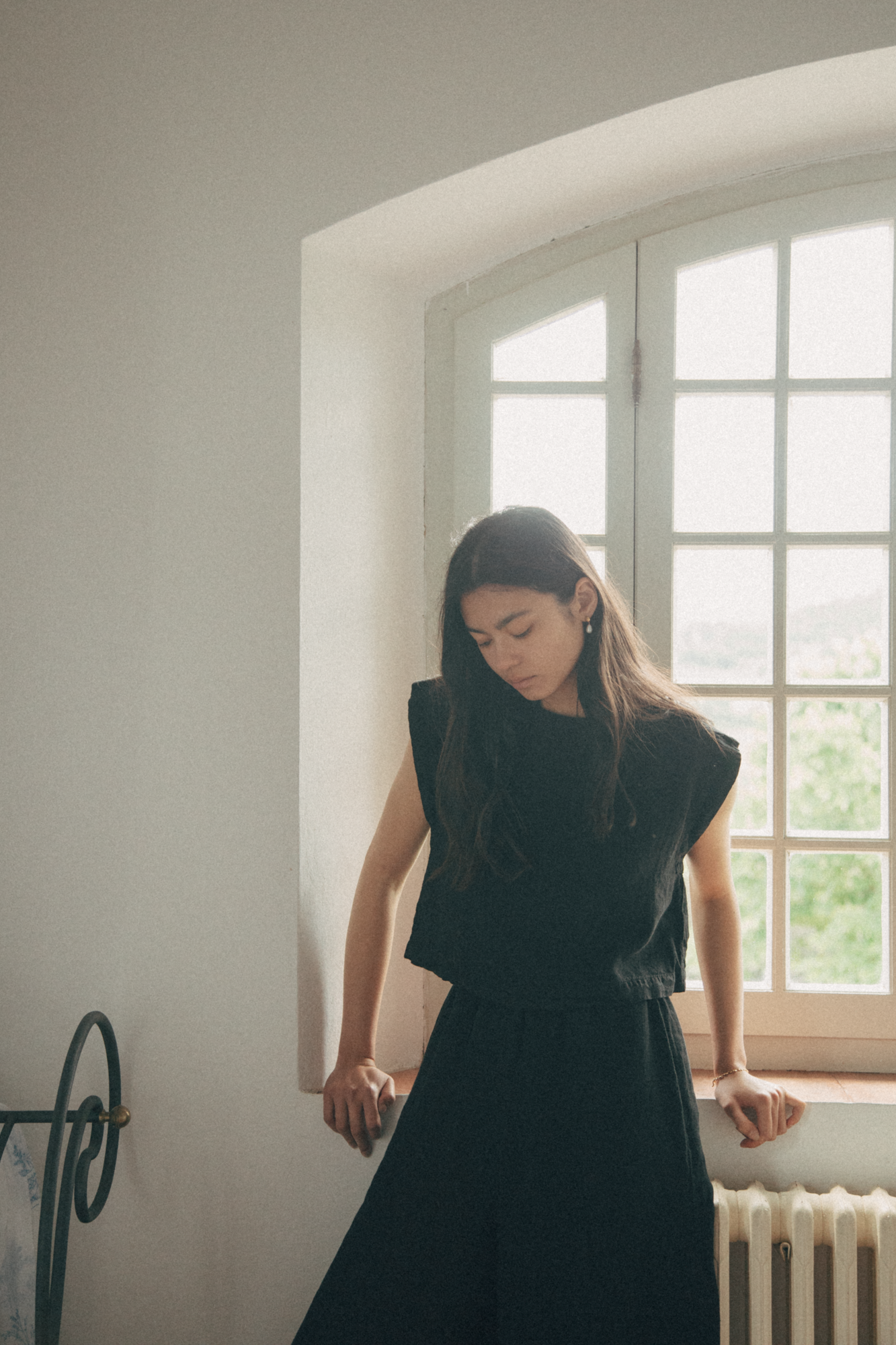 Model wearing the Valley Top in Noir by Gillian Stevens, front view beside a arched window
