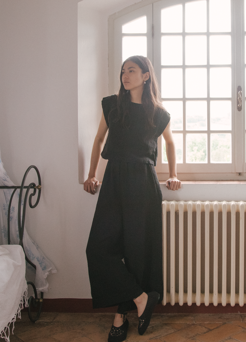 Model wearing the Valley Top in Noir by Gillian Stevens, full-length front view beside a sunlit window