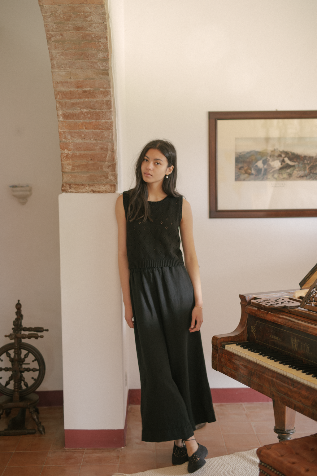 Model wearing the Ines Pant in Noir by Gillian Stevens, full-length front view beside a grand piano