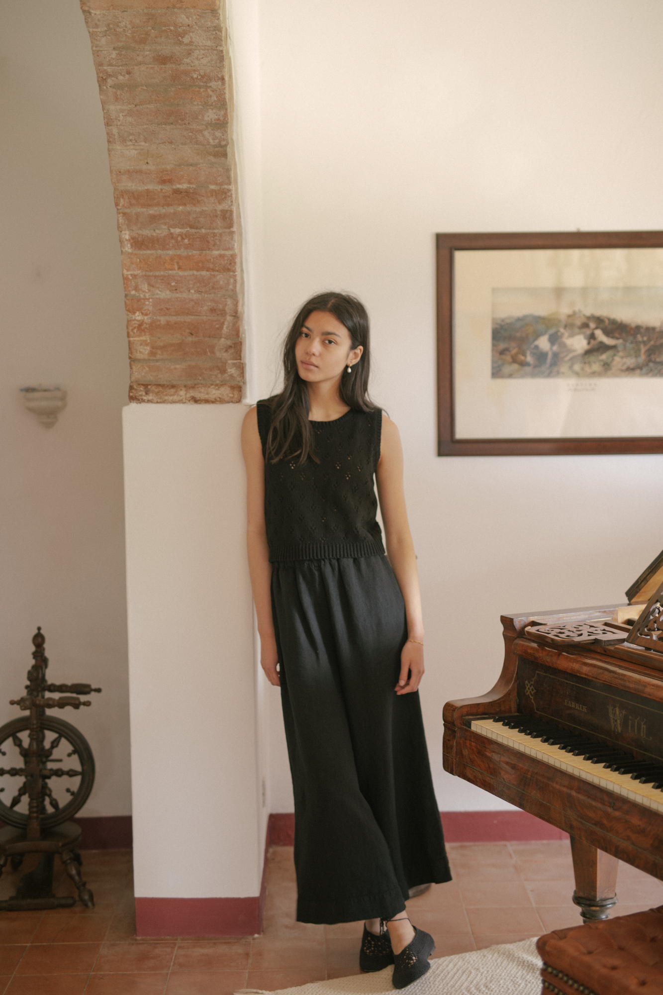 Model wearing the Ines Pant in Noir by Gillian Stevens, full-length front view beside a grand piano