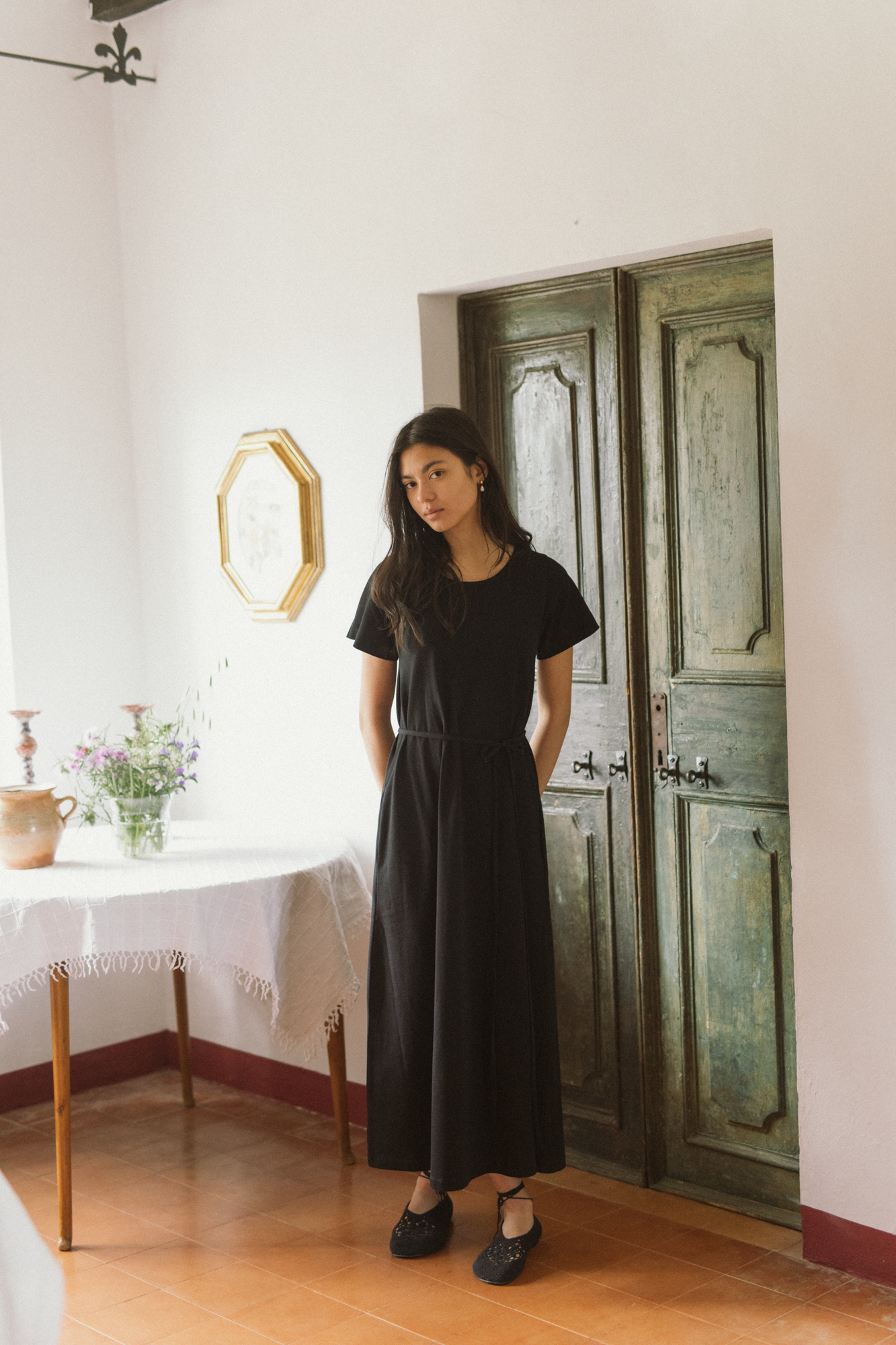 Model wearing the Palmer Dress in Noir by Gillian Stevens, front view in a rustic interior setting