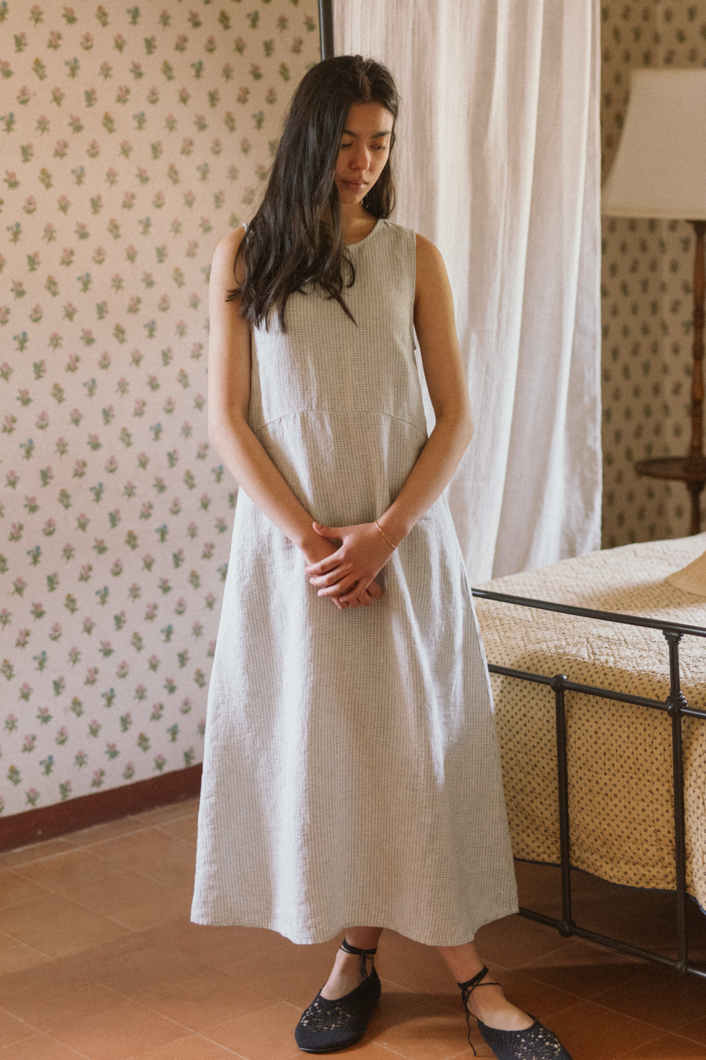 Model wearing the Paige Dress in Dusty Blue Plaid by Gillian Stevens, front view in a floral wallpapered room