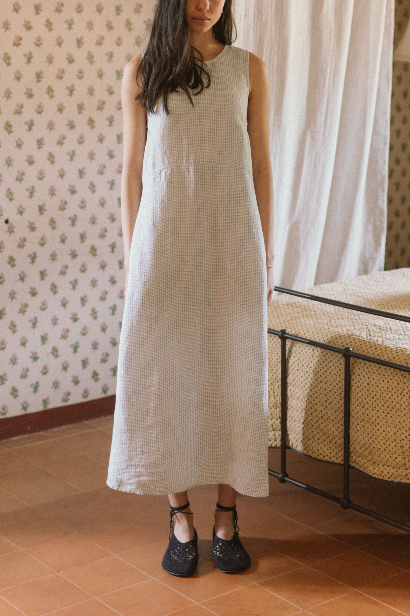 Model wearing the Paige Dress in Dusty Blue Plaid by Gillian Stevens, front view in a floral wallpapered room