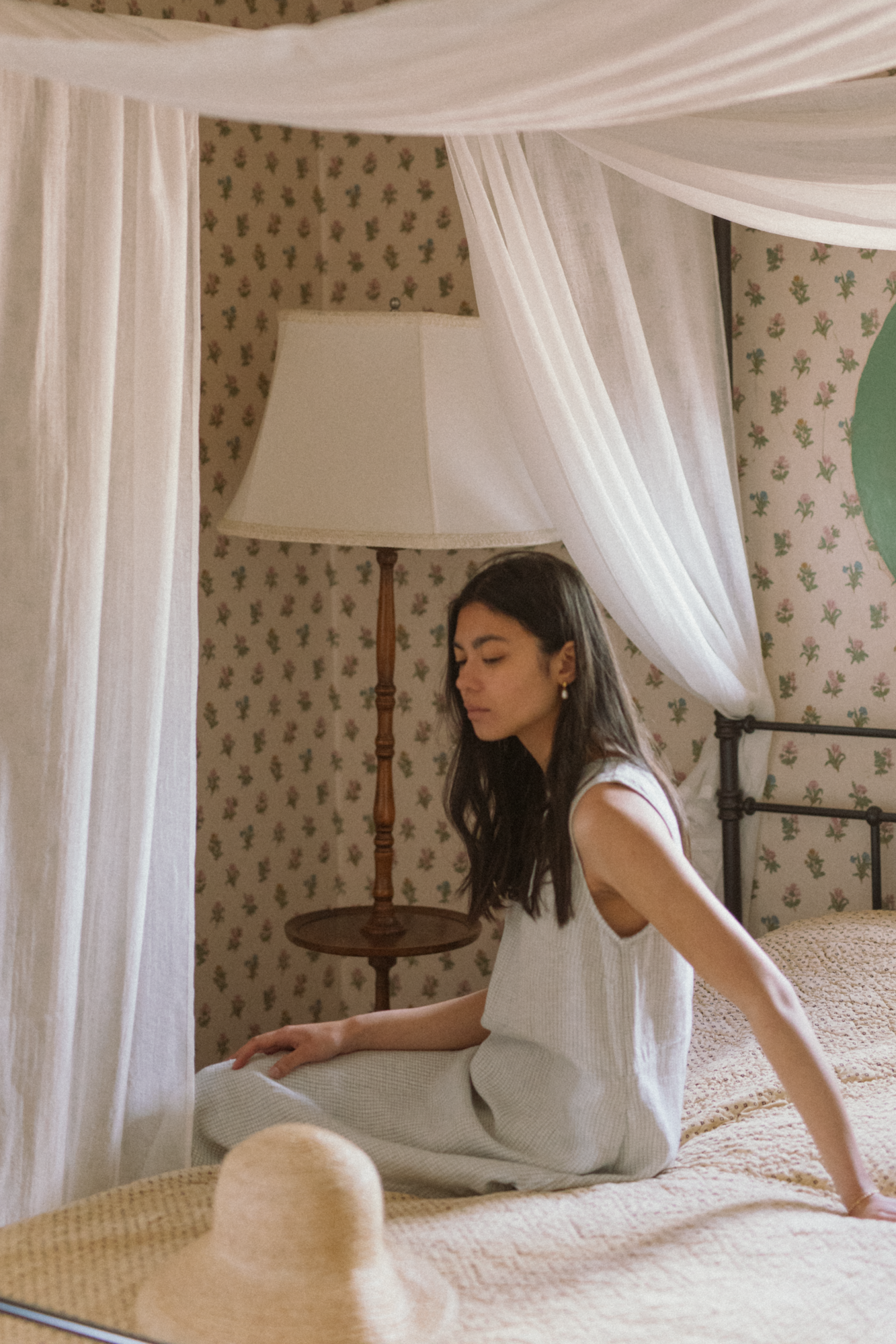 Model seated on a canopy bed wearing the Paige Dress in Dusty Blue Plaid by Gillian Stevens