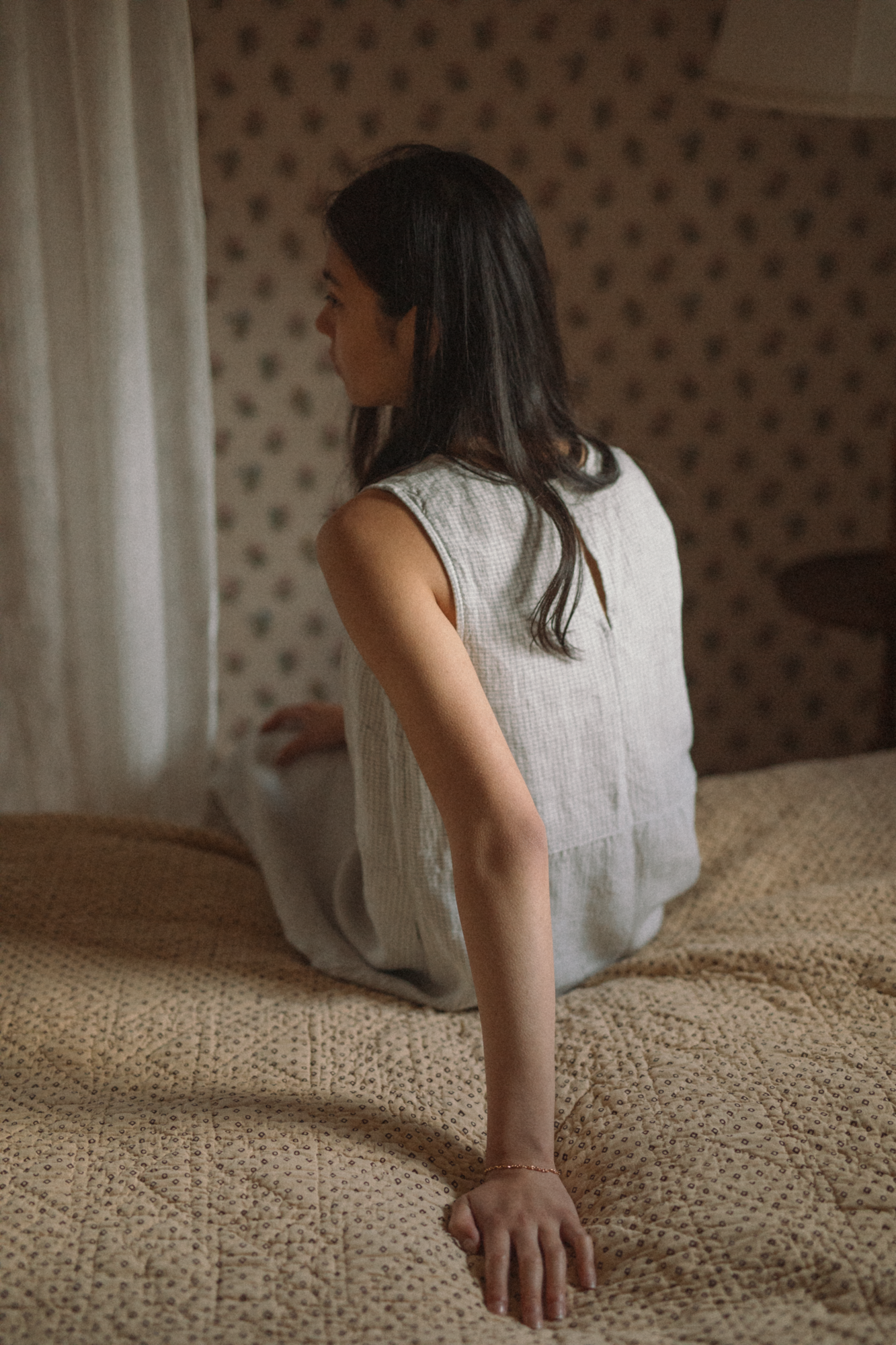Model seated on a bed wearing the Paige Dress in Dusty Blue Plaid by Gillian Stevens, back view