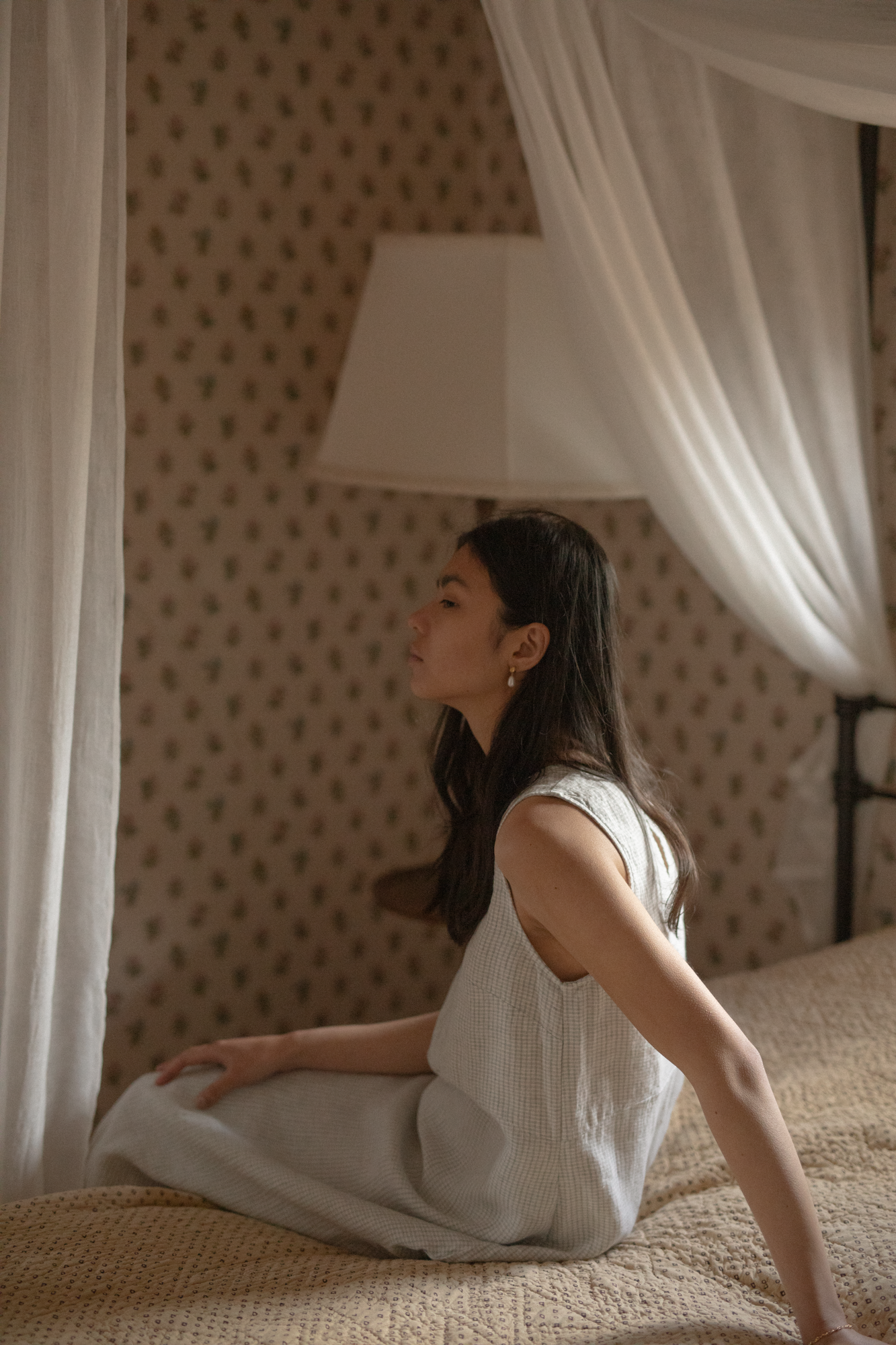 Model seated on a canopy bed in the Paige Dress in Dusty Blue Plaid by Gillian Stevens, side profile view