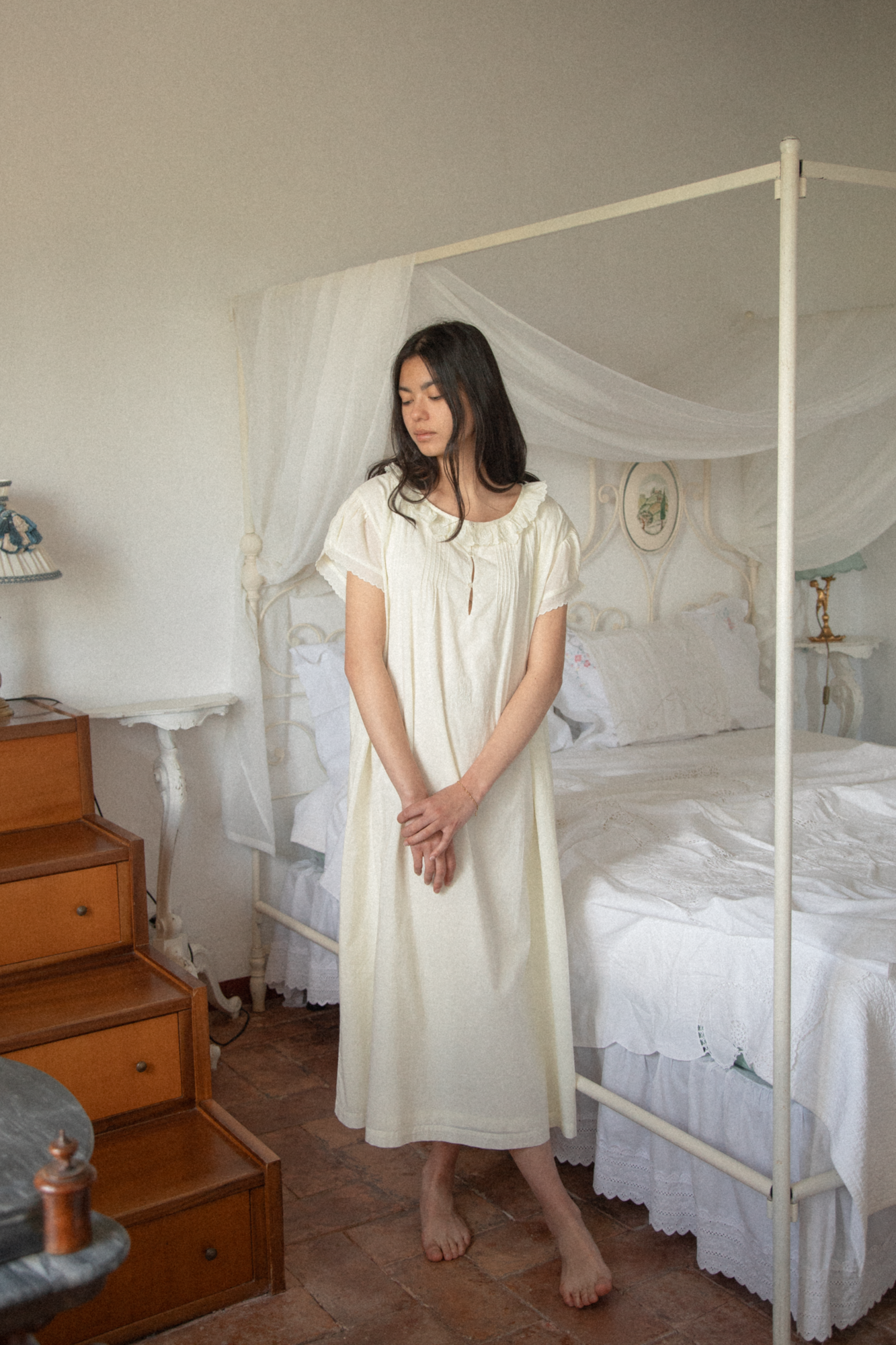 Model wearing the Clover Dress in Butter by Gillian Stevens, full-length front view in a styled bedroom setting